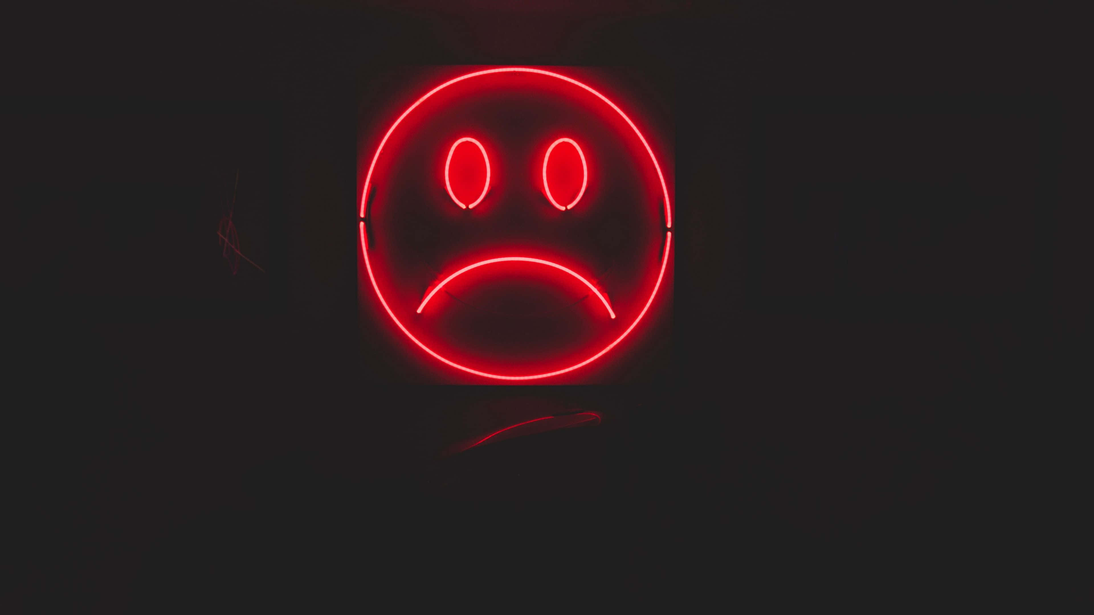 Depressing 桌布 壁紙 — 一個發光的紅色霓虹燈悲傷臉標誌在漆黑的背景上格外醒目。