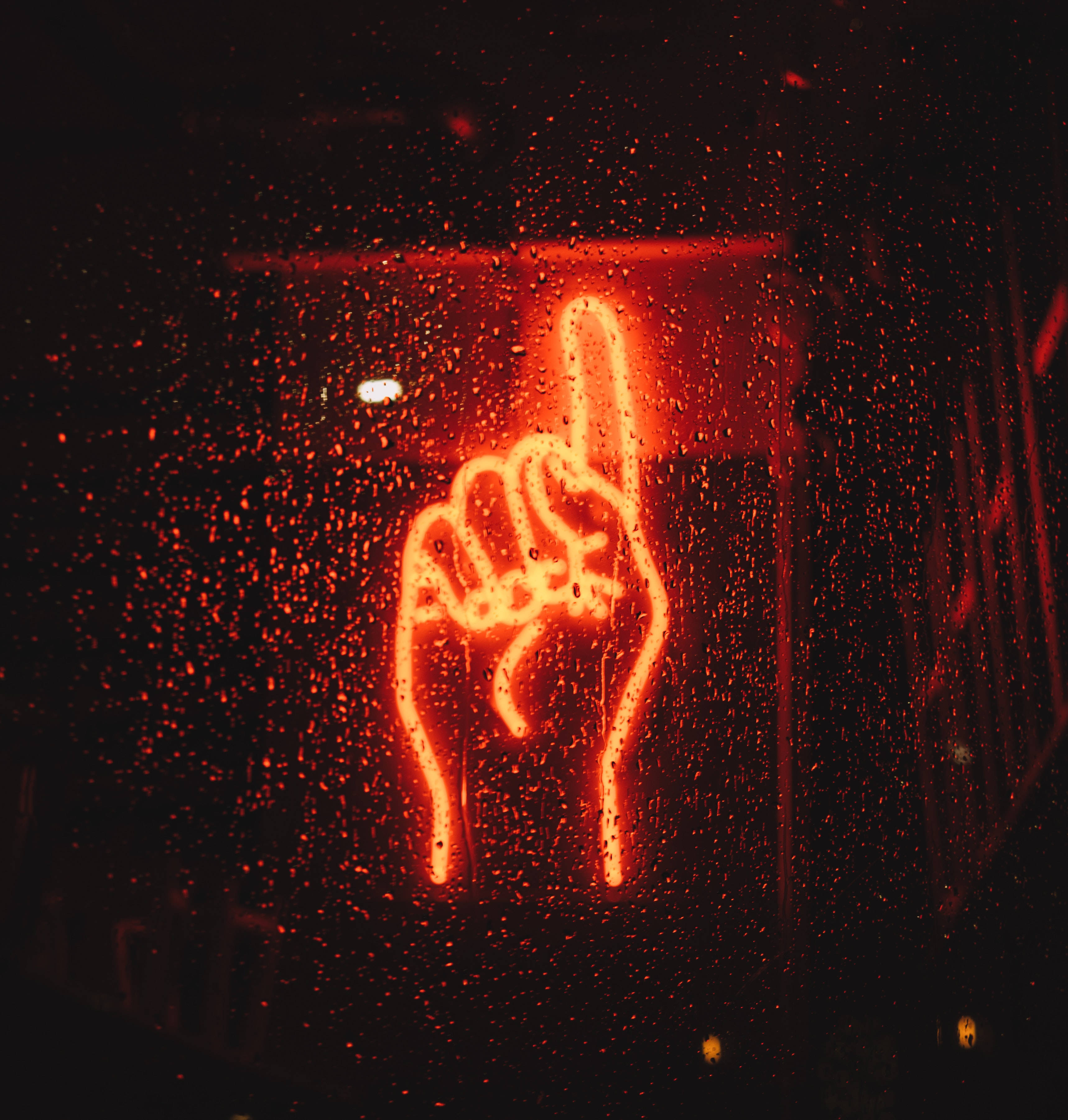neon sign 桌布 壁紙 — 一個發光的紅色霓虹燈手勢，食指豎起，在夜間透過佈滿雨點的窗戶閃耀。