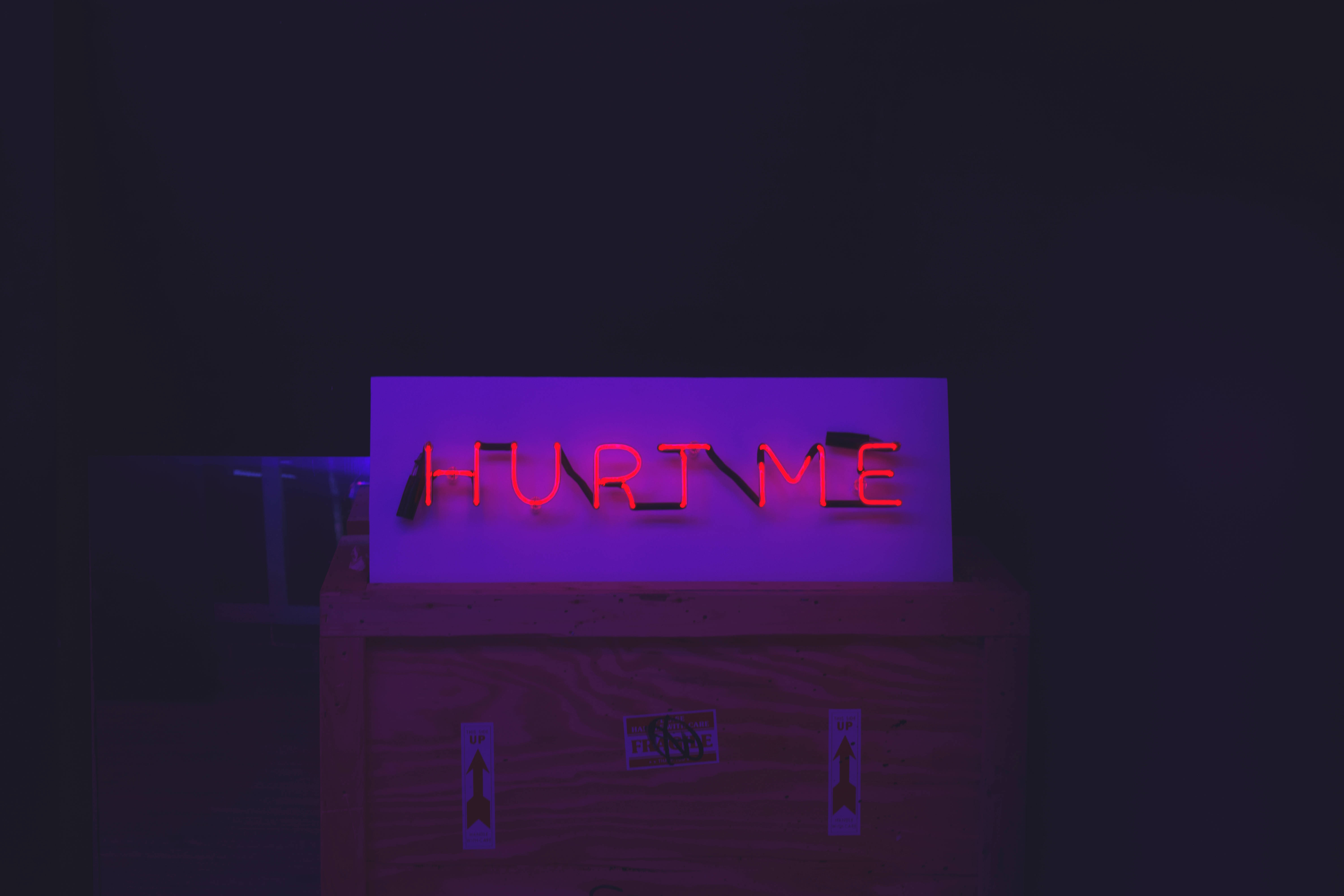 螢光綠 桌布 壁紙 — 一個發光的紅色霓虹燈牌，上面寫著「HURT ME」，在黑暗的房間裡將紫色色調投射在木箱上。