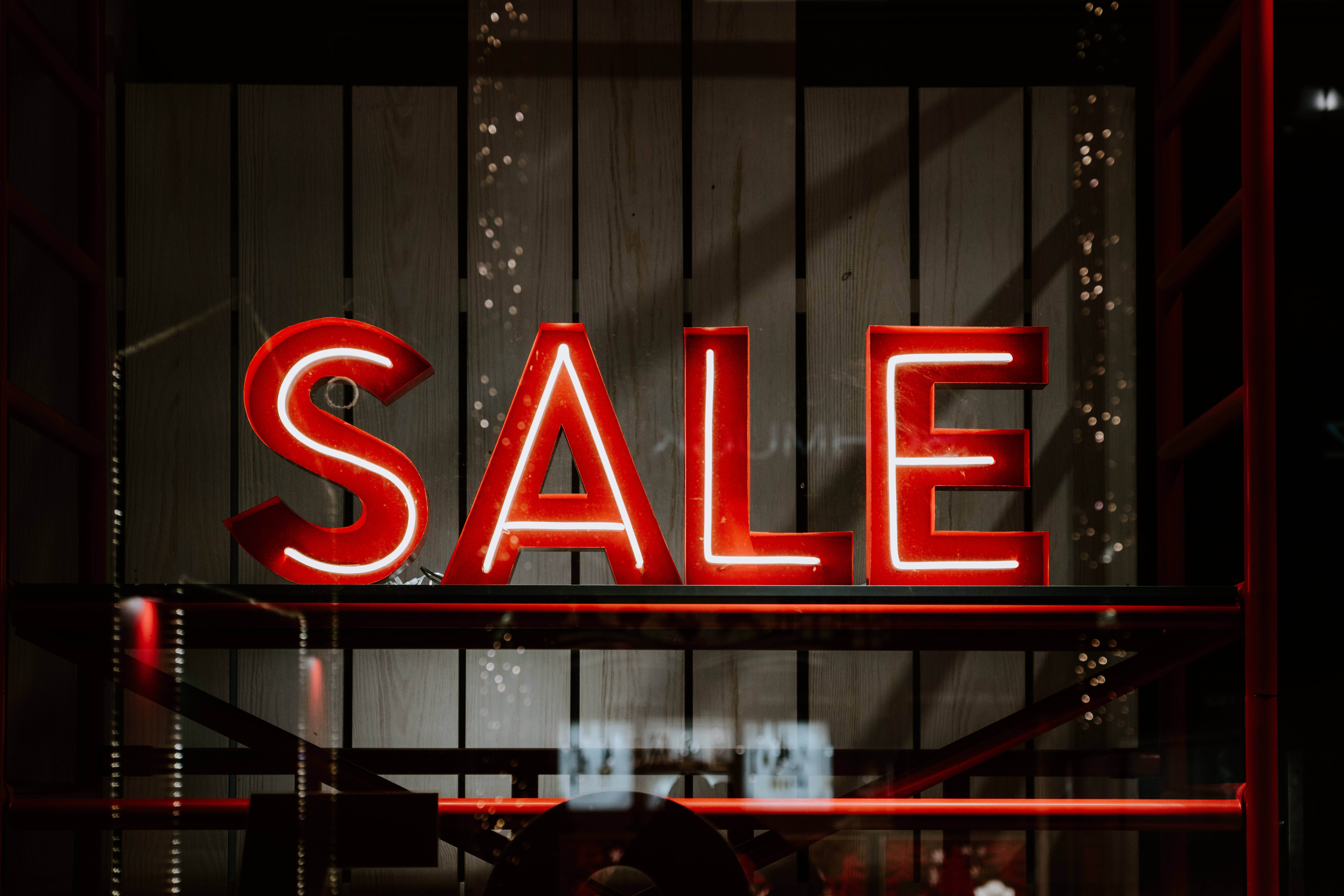 Sales 桌布 壁紙 — 一個發光的紅色霓虹燈牌，上面寫著 SALE，在商店櫥窗的深色木鑲板牆上明亮地閃耀。