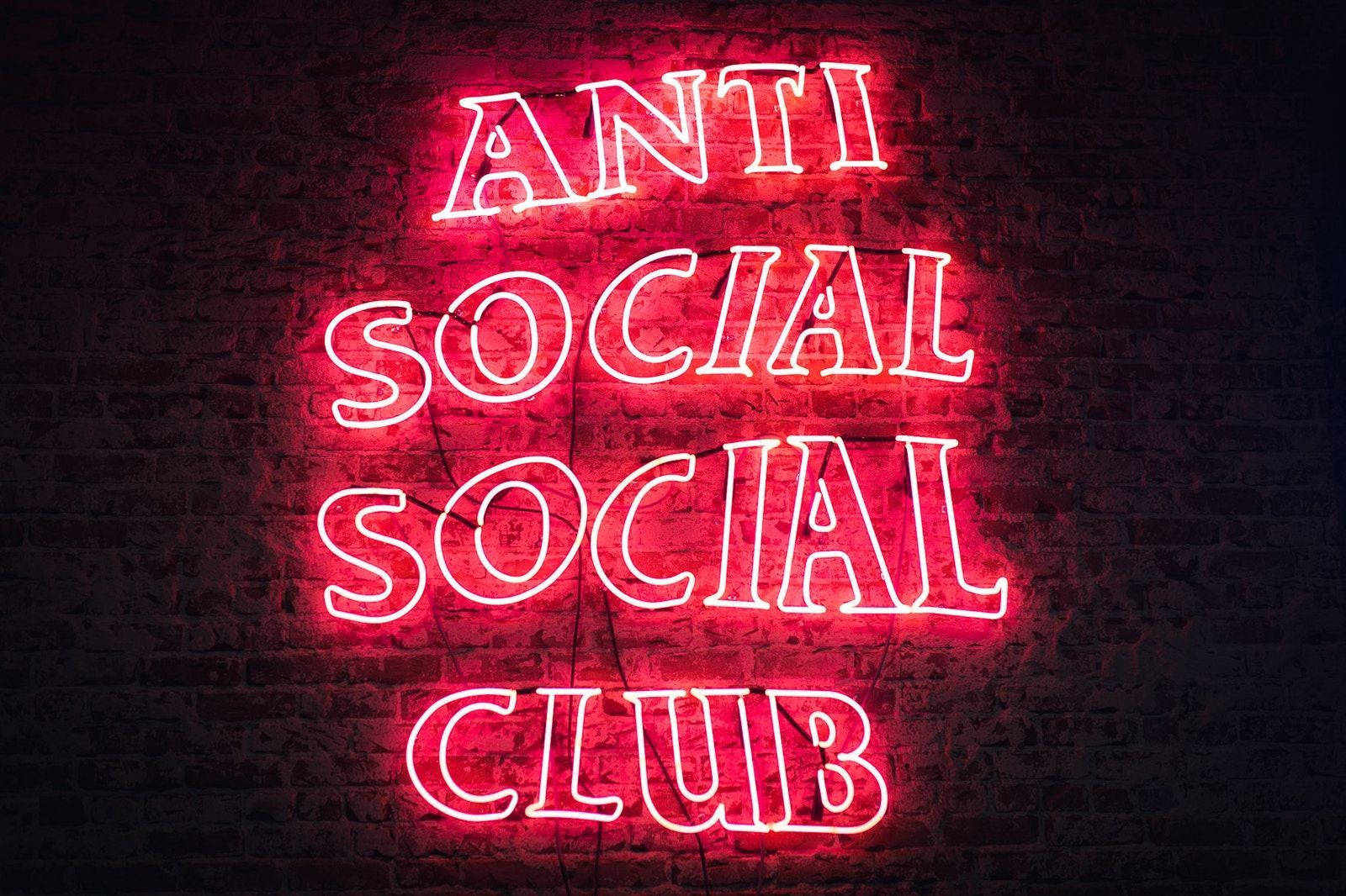 club 桌布 壁紙 — 一個發光的紅色霓虹燈牌，上面寫著「ANTI SOCIAL SOCIAL CLUB」，用充滿活力的光線照亮了深色磚牆。