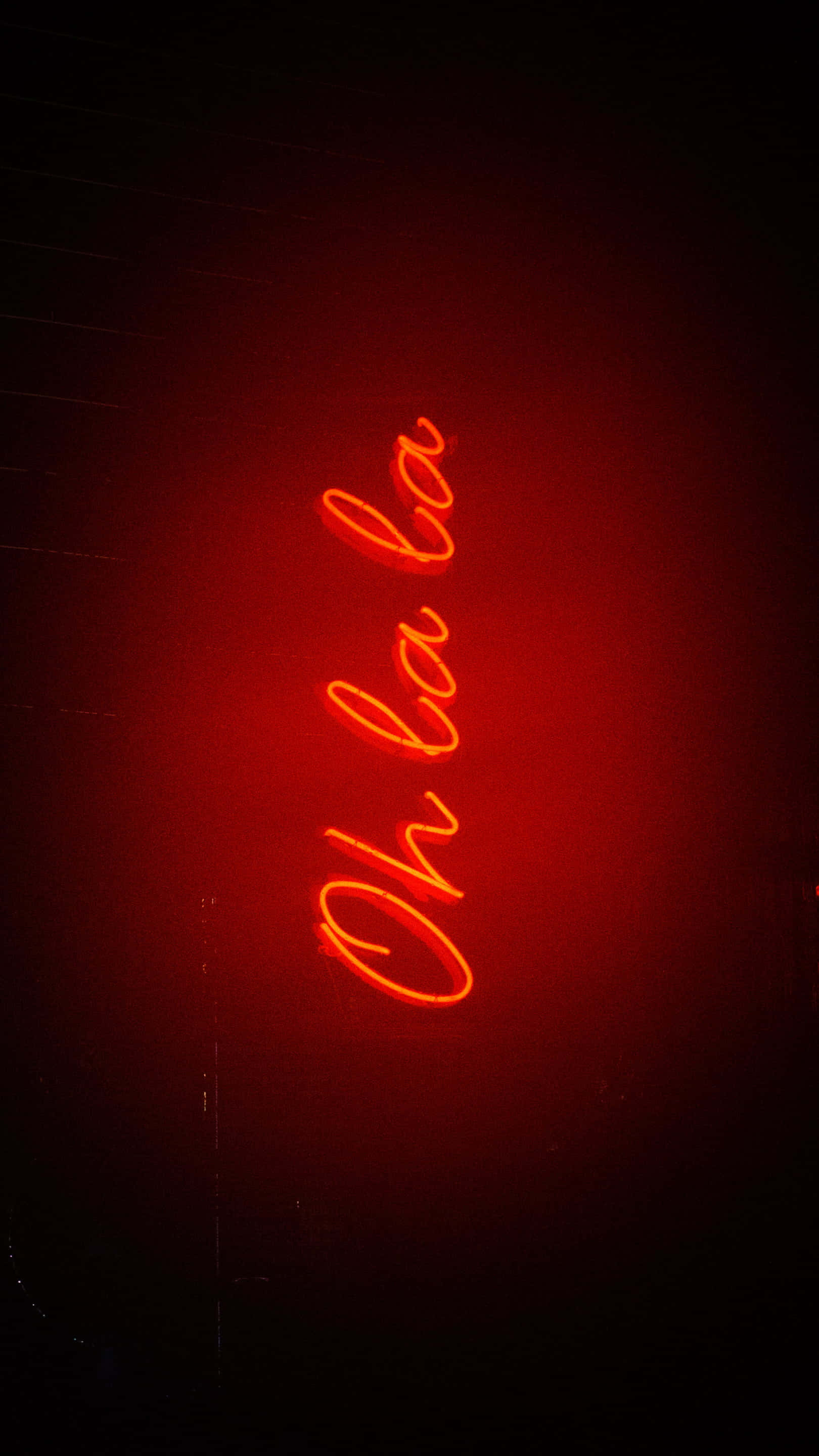 Dark Red Aesthetic 桌布 壁紙 — 一個發光的紅色霓虹燈牌，上面寫著「Oh la la」，在黑暗的背景下散發出溫暖的光芒。