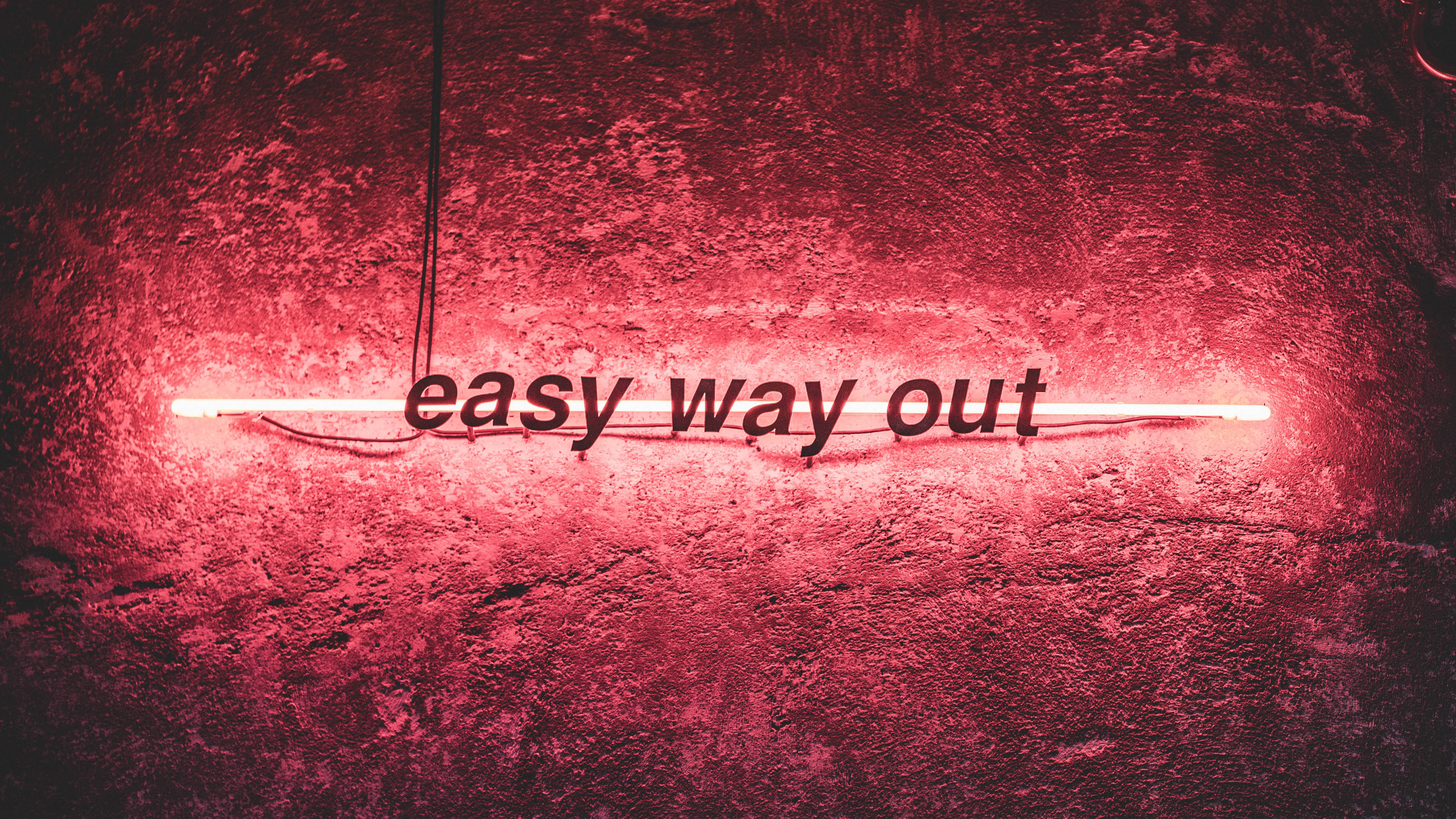 neon sign 桌布 壁紙 — 一個發光的紅色霓虹燈牌，上面寫著 'easy way out'，在粗糙的紋理牆上投射出溫暖的光芒。