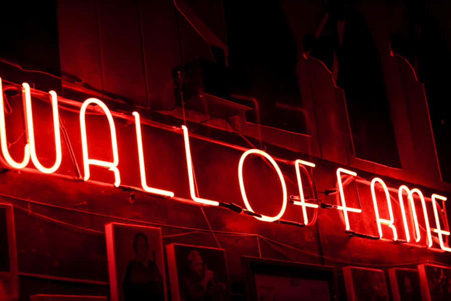 Neon Lights Aesthetic 桌布 壁紙 — 一個發光的紅色霓虹燈牌，上面寫著「WALL OF FAME」，照亮了下方掛有裱框照片的深色牆壁。