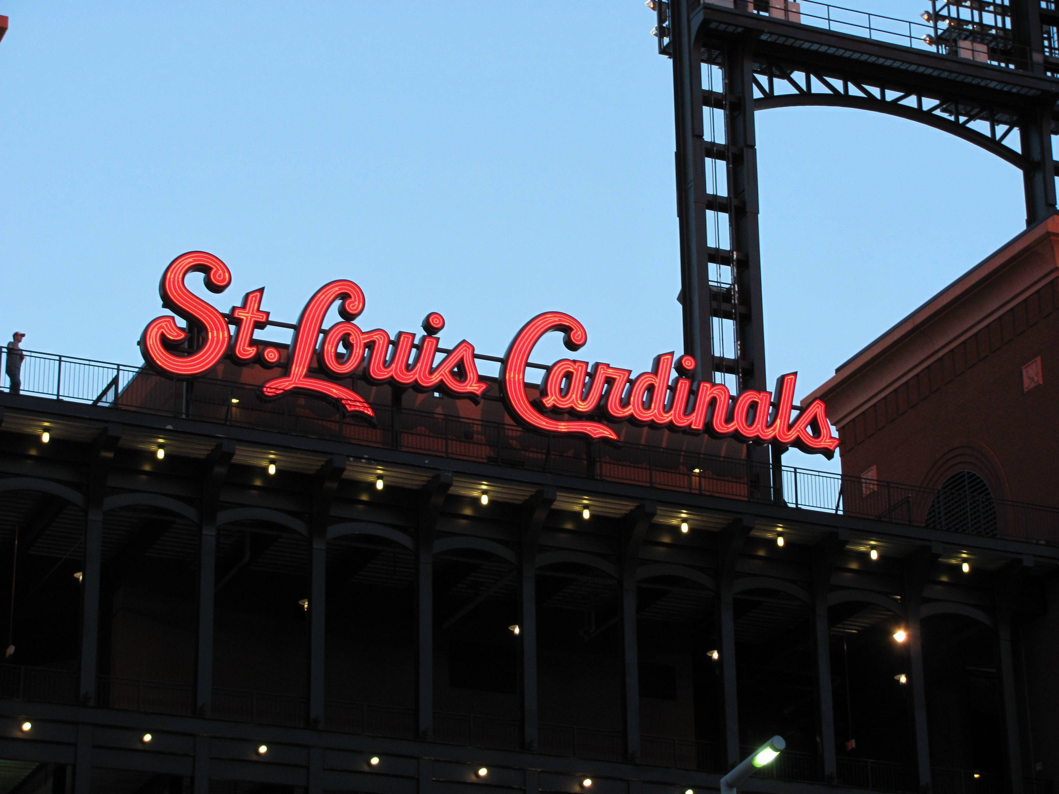 Cardinals 桌布 壁紙 — 一個發光的紅色霓虹燈牌，上面寫著 St Louis Cardinals，照亮了球場的外牆，背景是黃昏的天空。