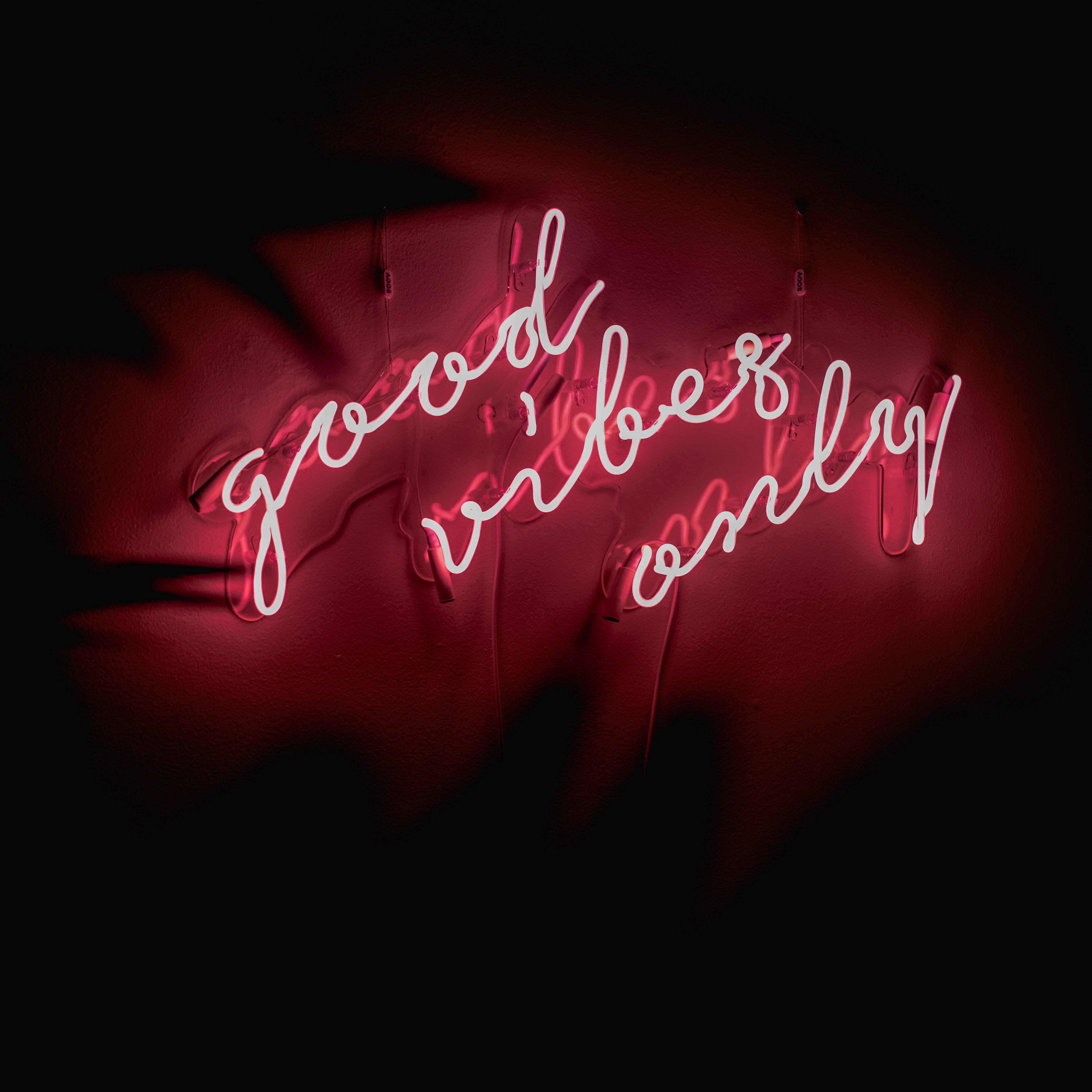 Hello 桌布 壁紙 — 一個發光的紅色霓虹燈牌，上面寫著「good vibes only」，在深色紋理牆上投射出溫暖的光芒。