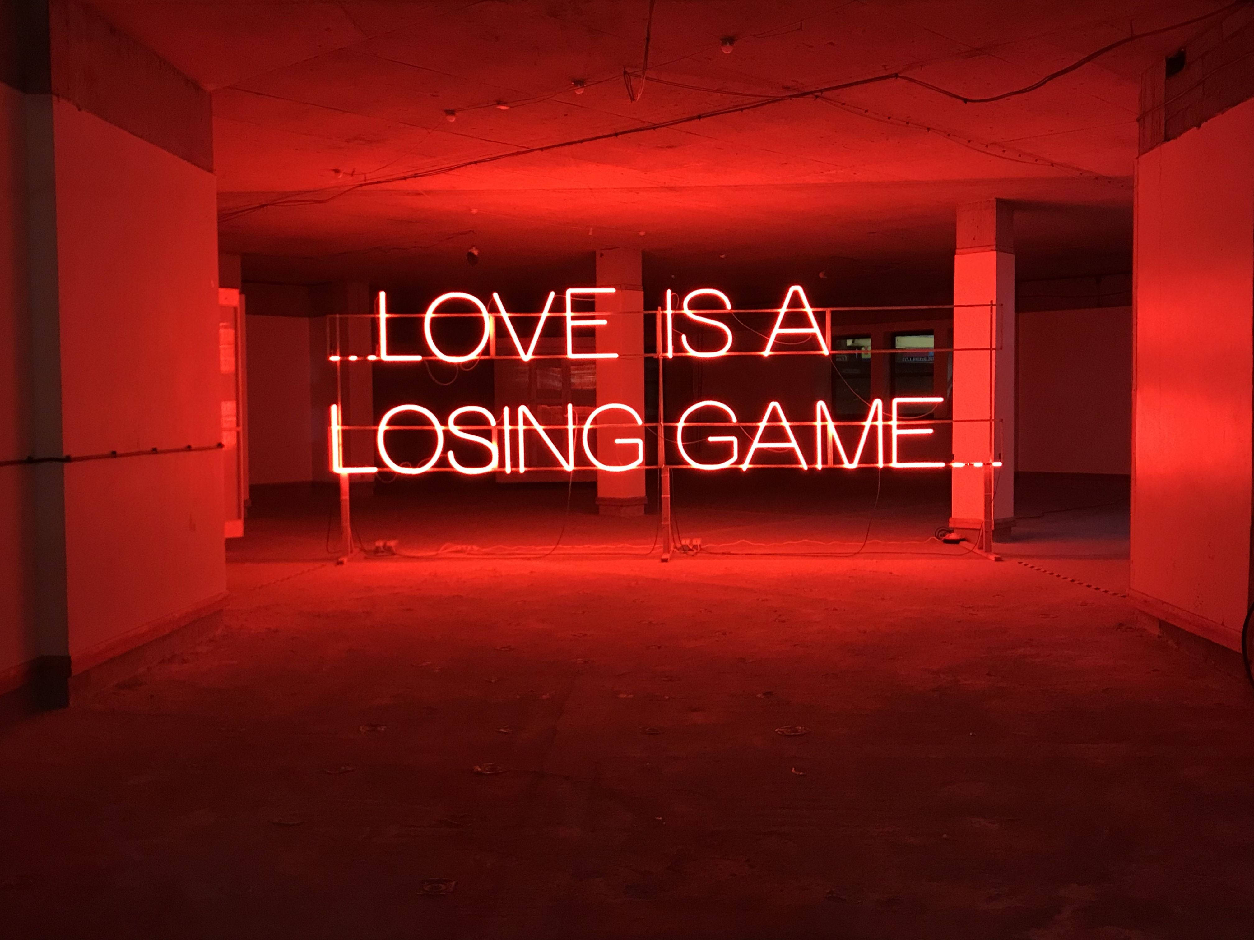美學 桌布 壁紙 — 一個發光的紅色霓虹燈牌，上面寫著「LOVE IS A LOSING GAME」，照亮了一個廢棄的混凝土房間。