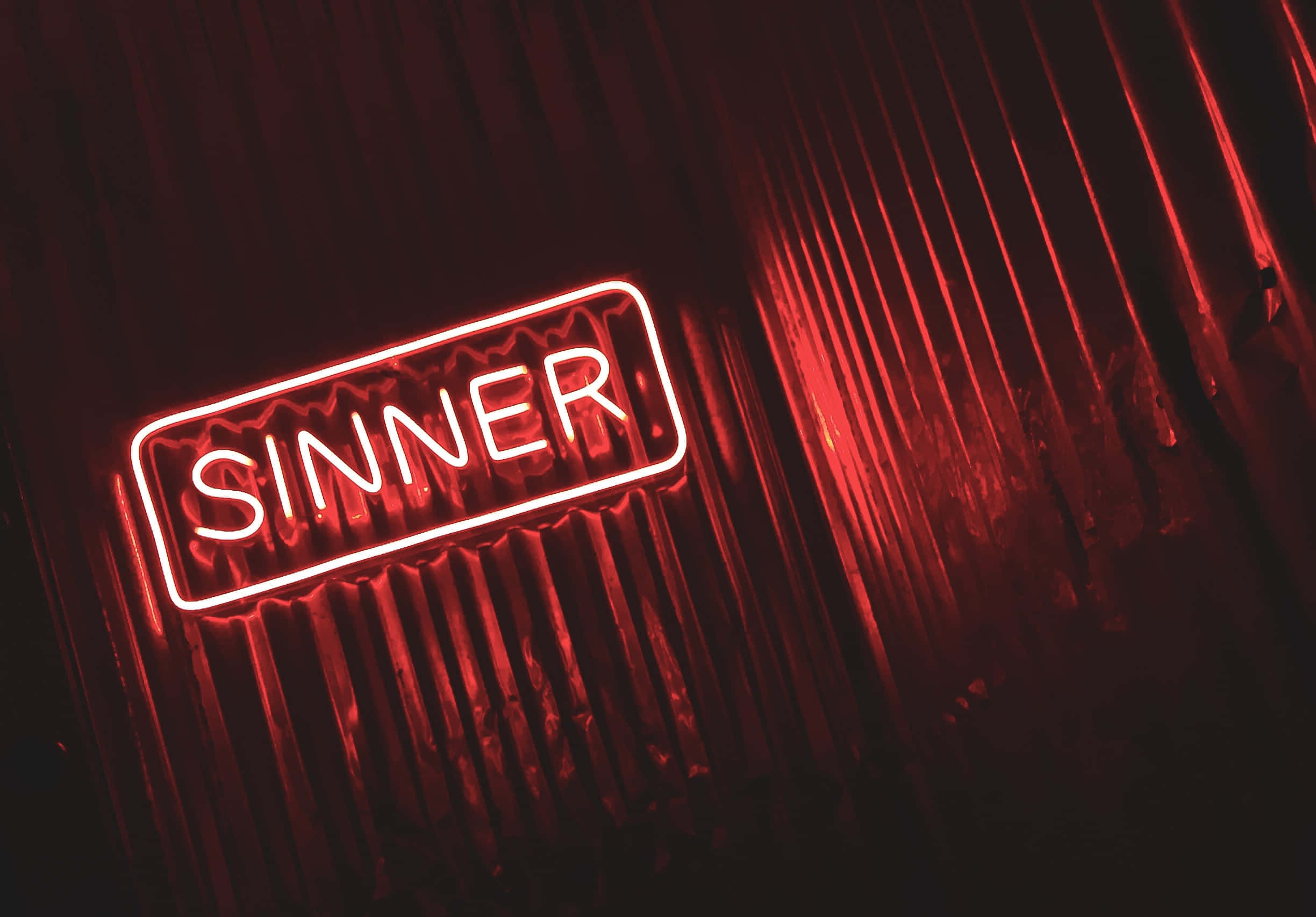 Neon Red Aesthetic 桌布 壁紙 — 一個發光的紅色霓虹燈牌，上面寫著「SINNER」，在昏暗的空間中將溫暖的光線投射在波紋金屬牆上。