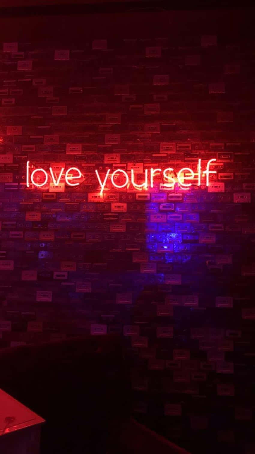 紅色動圖 桌布 壁紙 — 一個發光的紅色霓虹燈牌，上面寫著 love yourself，照亮了佈滿卡式錄音帶的黑暗牆壁。