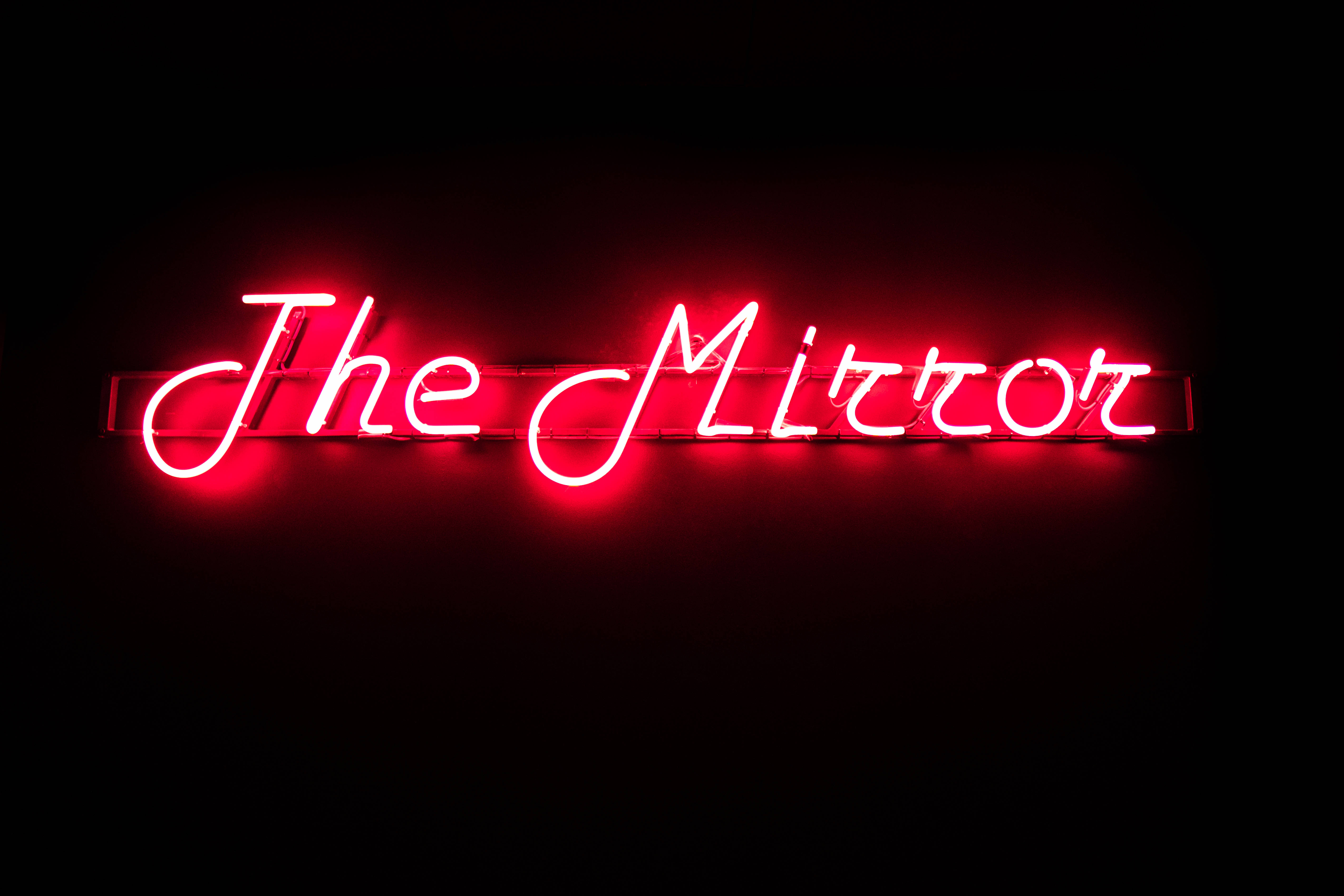 字型 桌布 壁紙 — 一個發光的紅色霓虹燈牌，上面寫著「The Mirror」，在漆黑的背景下投射出溫暖的光芒。