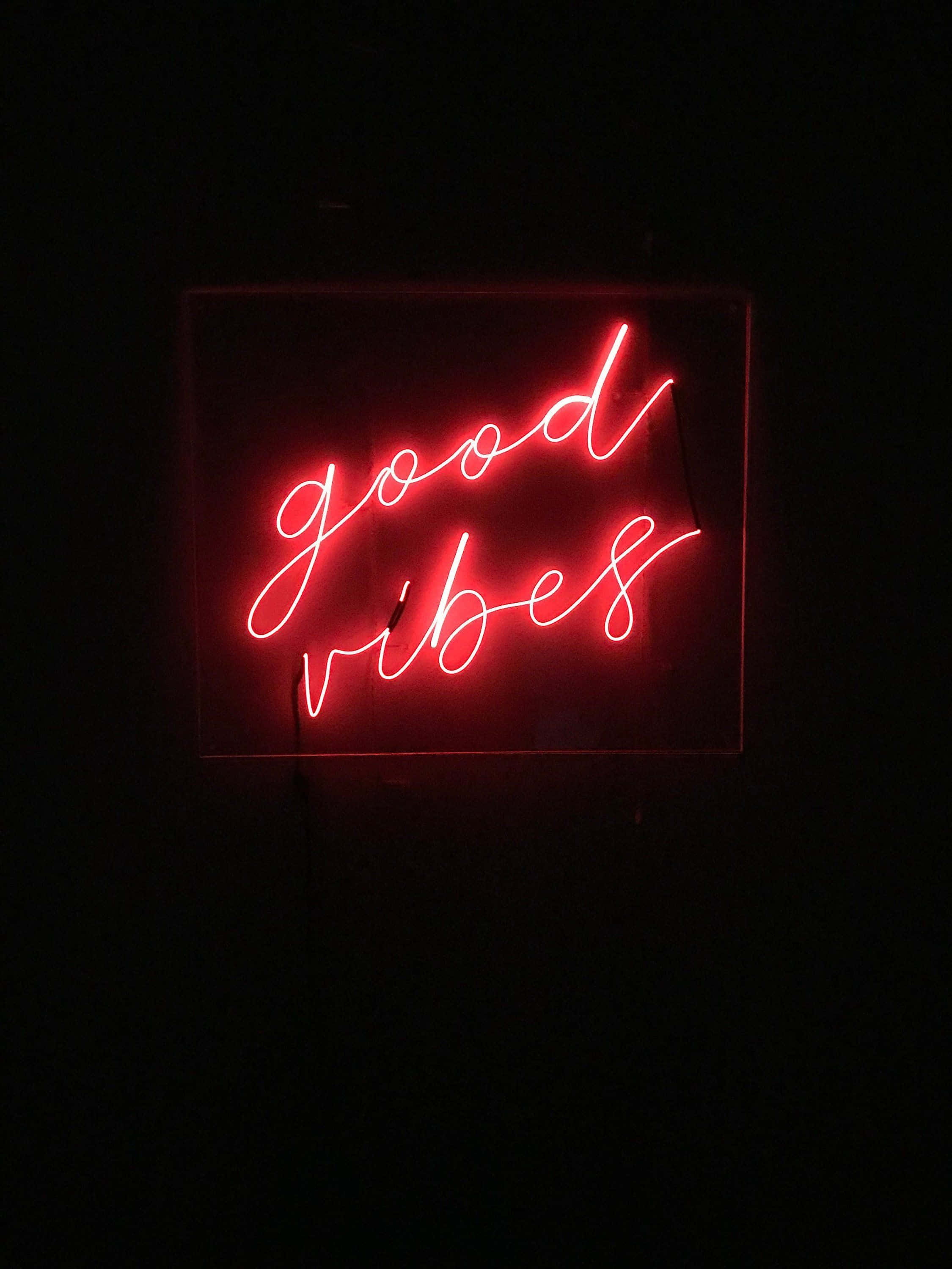 Red Neon 桌布 壁紙 — 一個發光的紅色霓虹燈牌，上面有草書 'good vibes' 文字，在漆黑的背景下照亮。