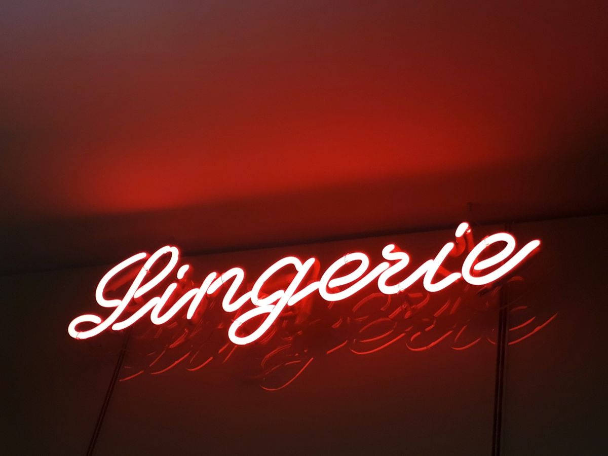 美學 桌布 壁紙 — 一個發光的紅色霓虹燈牌，以草書拼寫「Lingerie」，在黑暗的天花板上投射出溫暖的環境光。