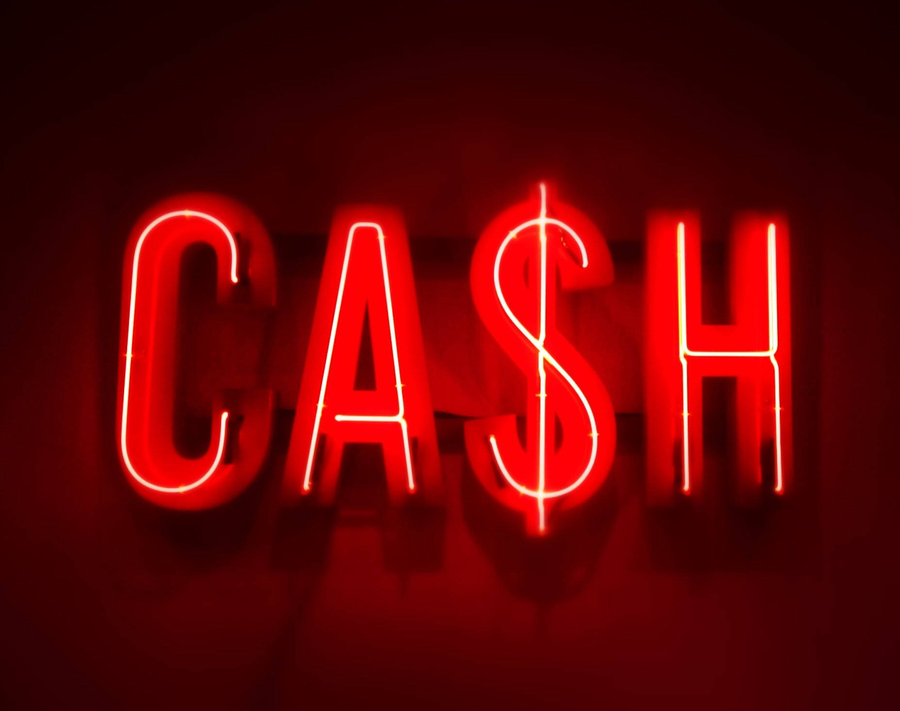 Money Sign 桌布 壁紙 — 一個發光的紅色霓虹燈牌，拼出 'CASH'，其中 'S' 被美元符號取代，在黑暗背景上投射出溫暖的光芒。