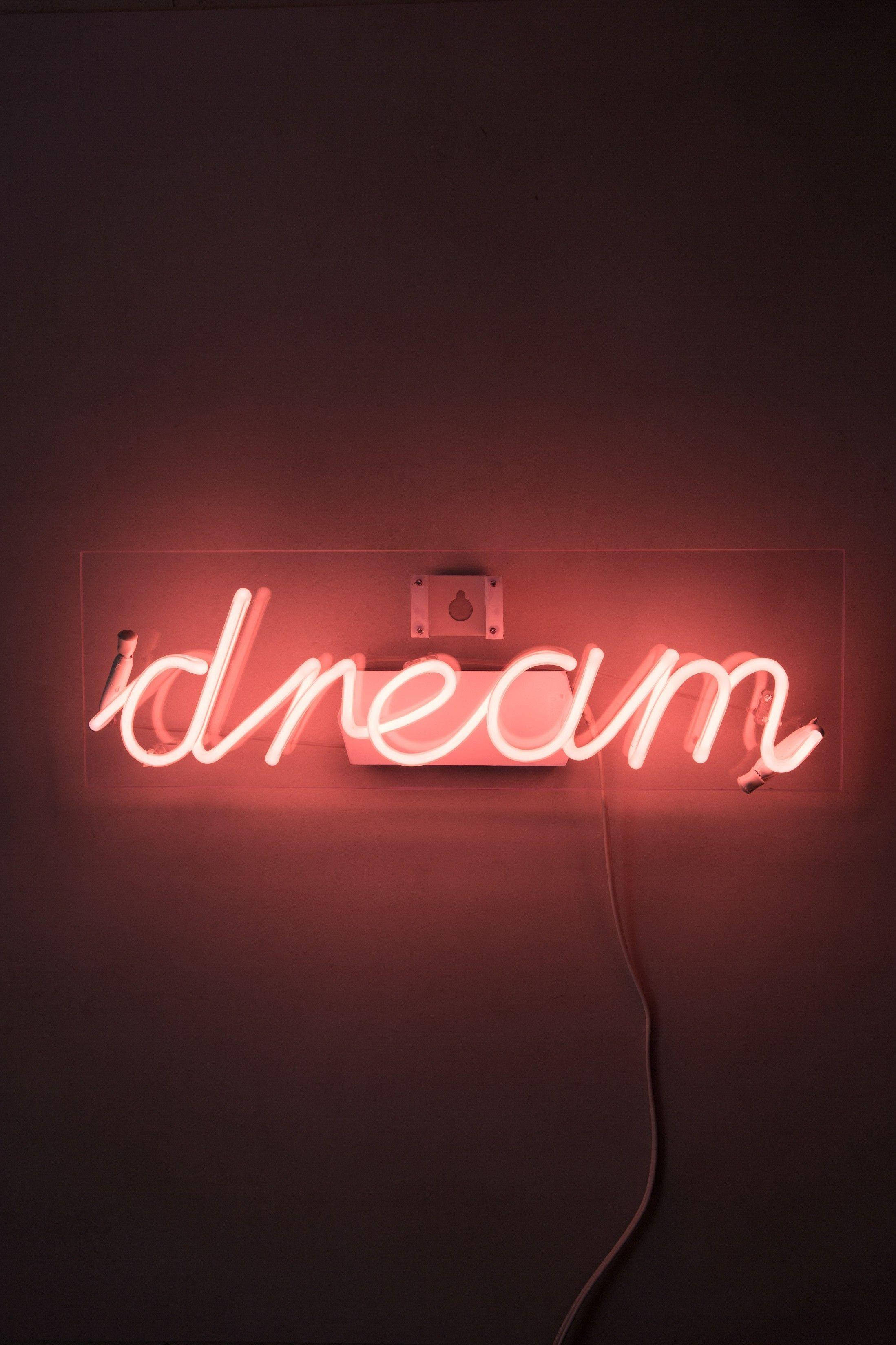 紅色 iPhone 桌布 壁紙 — 一個發光的紅色霓虹燈牌，拼出「dream」字樣，在極簡風格的環境中將溫暖的光線投射在深色牆壁上。
