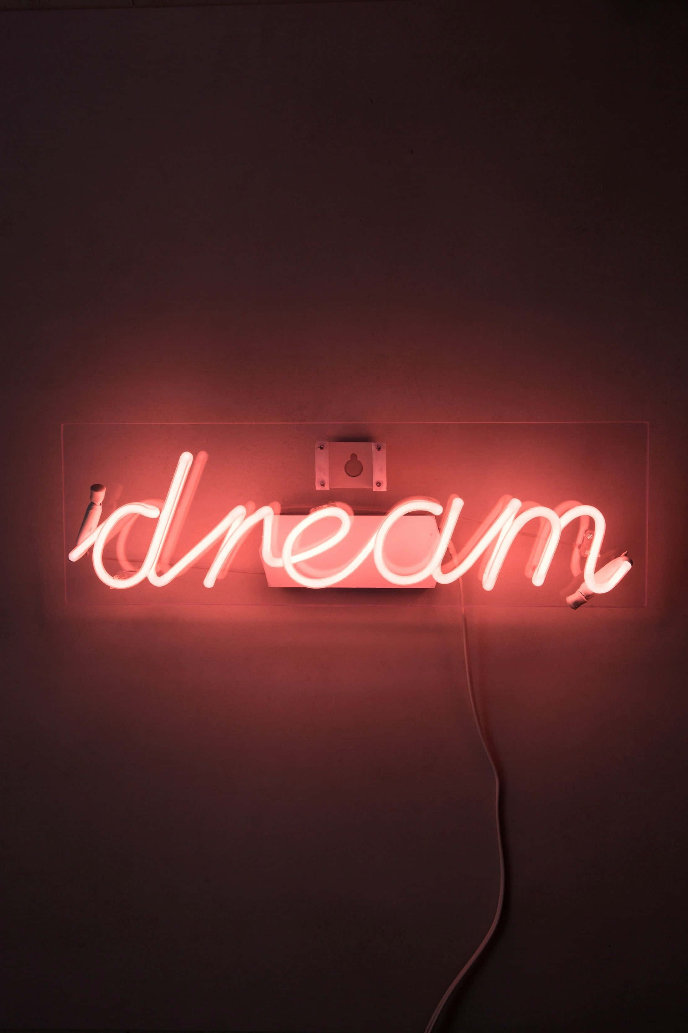 Neon Red Aesthetic 桌布 壁紙 — 一個發光的紅色霓虹燈牌，拼寫著「dream」，向暗牆投射溫暖的光線，並帶有可見的電源線。