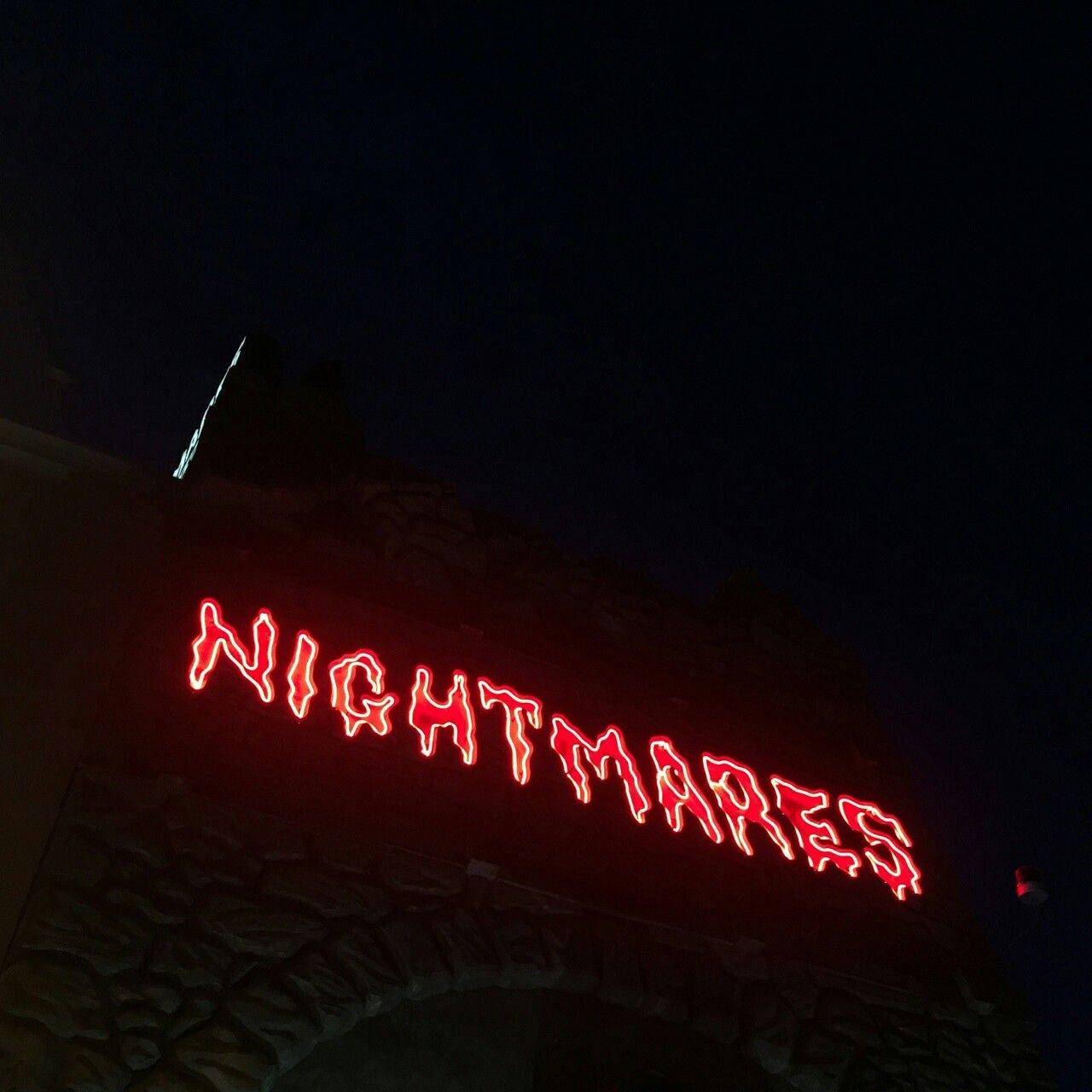 紅色動圖 桌布 壁紙 — 一個發光的紅色霓虹燈牌，拼寫著 nightmares，在漆黑的夜空下拱形跨越石頭入口。