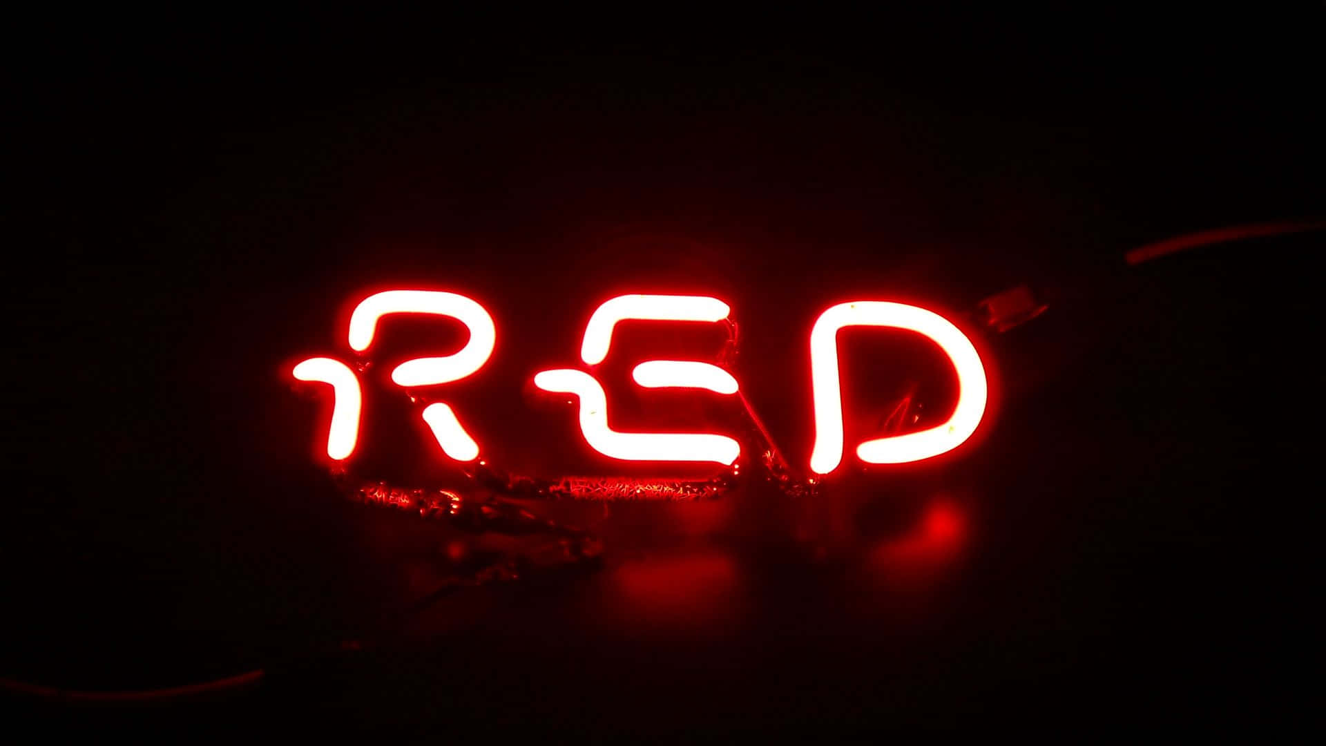 紅色美學動圖 桌布 壁紙 — 一個發光的紅色霓虹燈牌，拼寫著「RED」，以鮮豔的光芒照亮黑暗的背景。