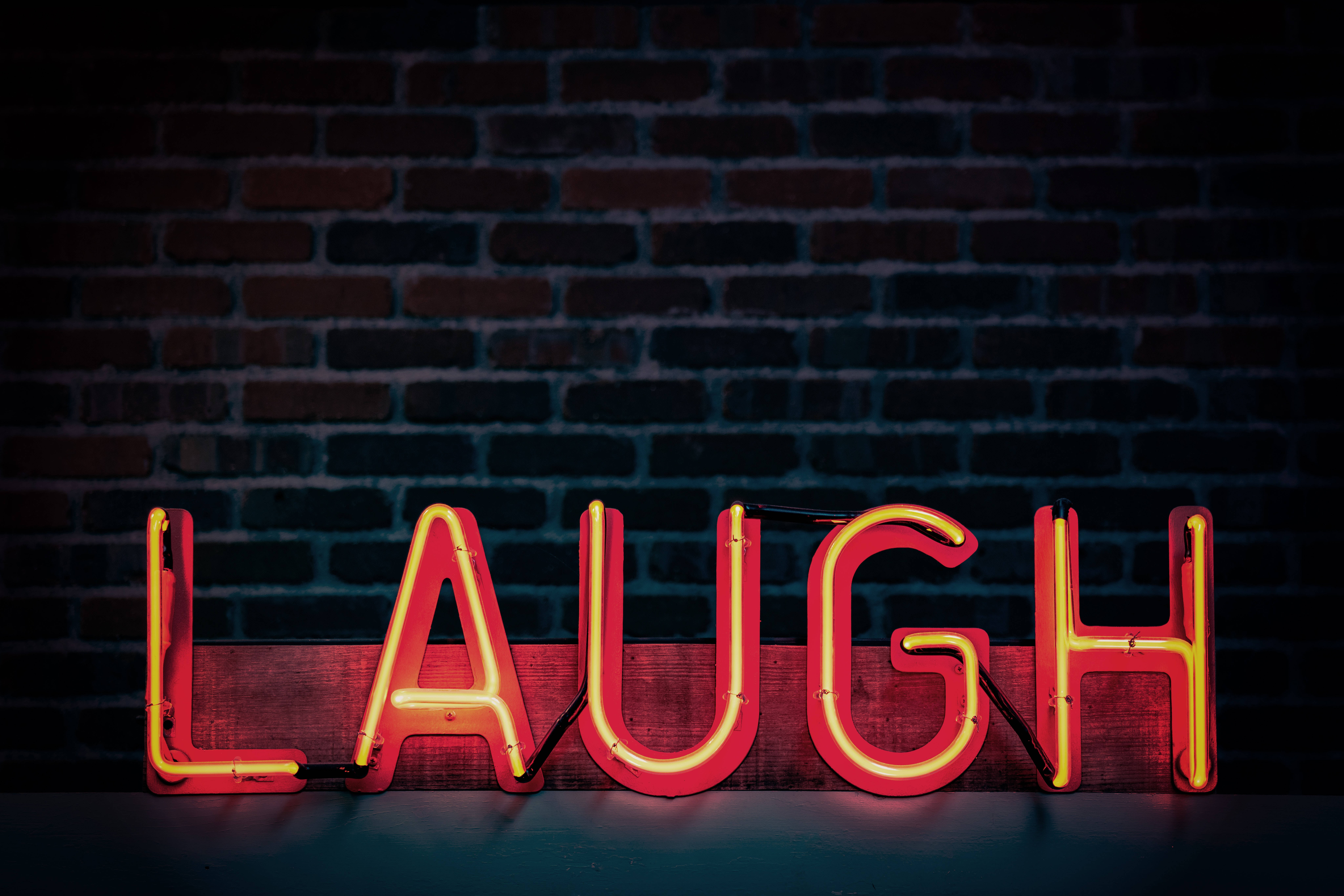 Brick 桌布 壁紙 — 一個發光的紅色霓虹燈牌，拼寫著 LAUGH，放在一塊木板上，靠著深色磚牆。