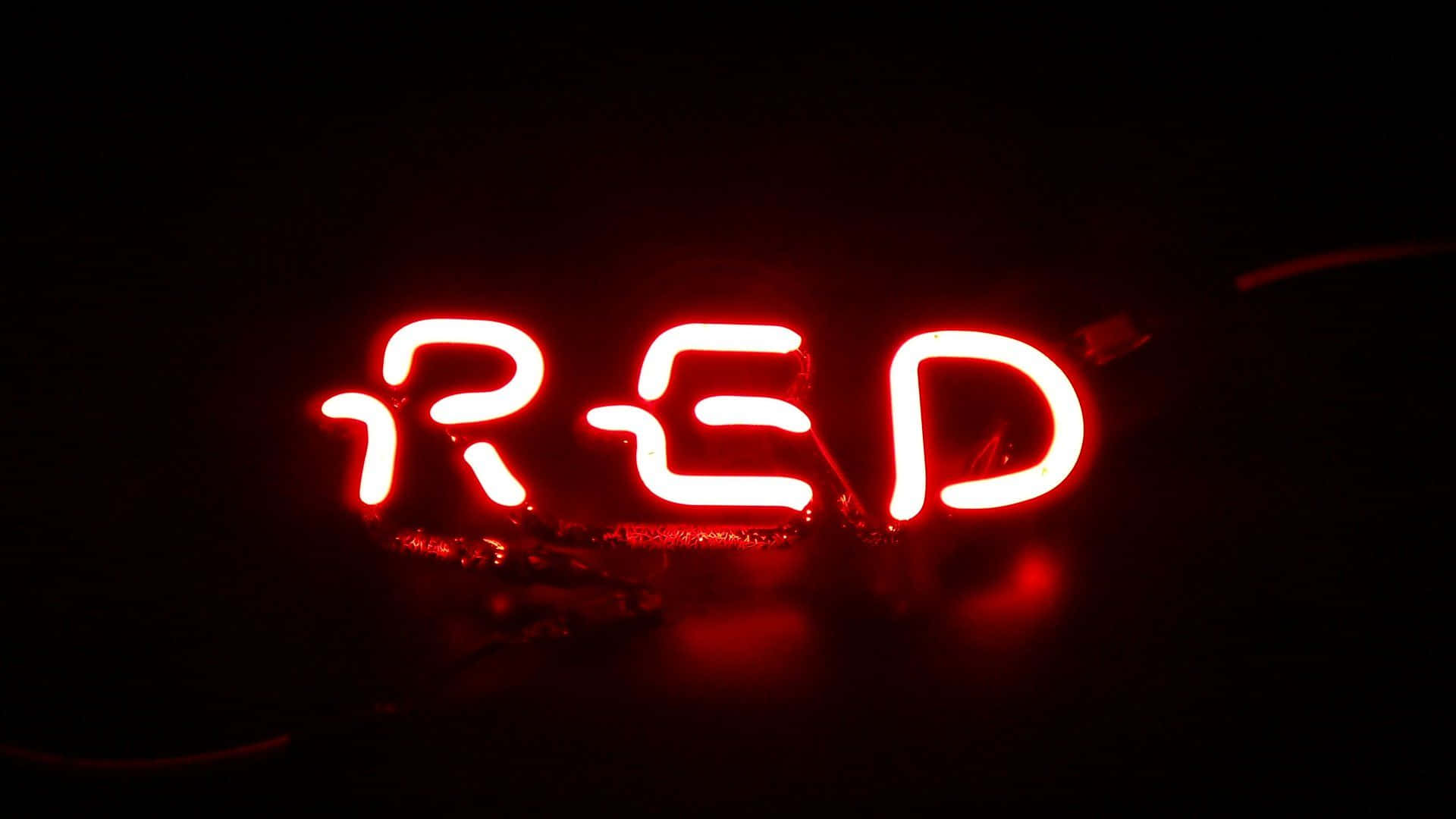 紅色動圖 桌布 壁紙 — 一個發光的紅色霓虹燈牌，拼寫著 'RED'，在漆黑的背景上脈動，帶有可見的電線和反射。