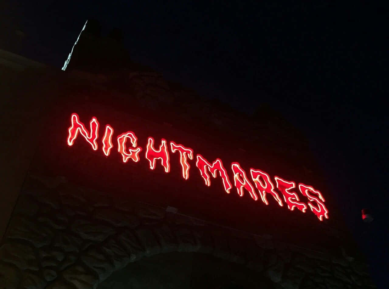 美學 桌布 壁紙 — 一個發光的紅色霓虹燈牌，拼寫著nightmares，在夜晚對著黑暗的石拱門投射出詭異的光芒。