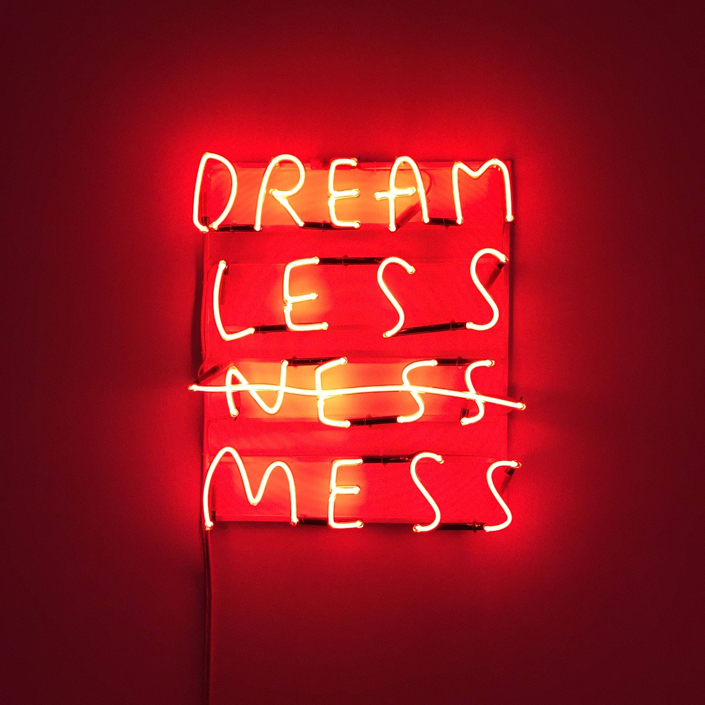 霓虹 桌布 壁紙 — 一個發光的紅色霓虹燈牌在深紅色牆上顯示 'DREAM LESS MESS'，其中 'NESS' 被劃掉。