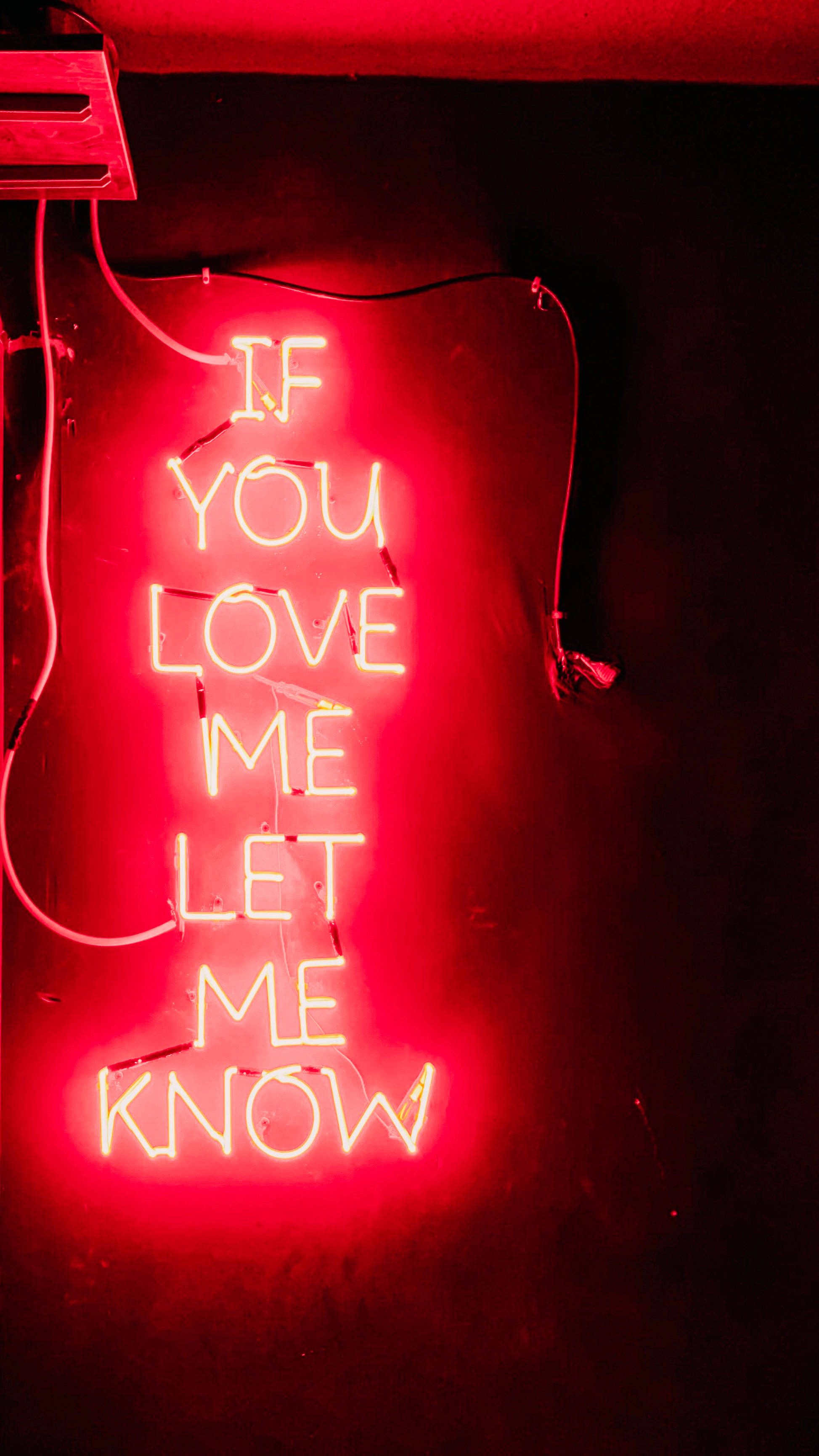 iPhone 6 桌布 壁紙 — 一個發光的紅色霓虹燈牌寫著 'IF YOU LOVE ME LET ME KNOW'，映在昏暗空間的深色牆上。
