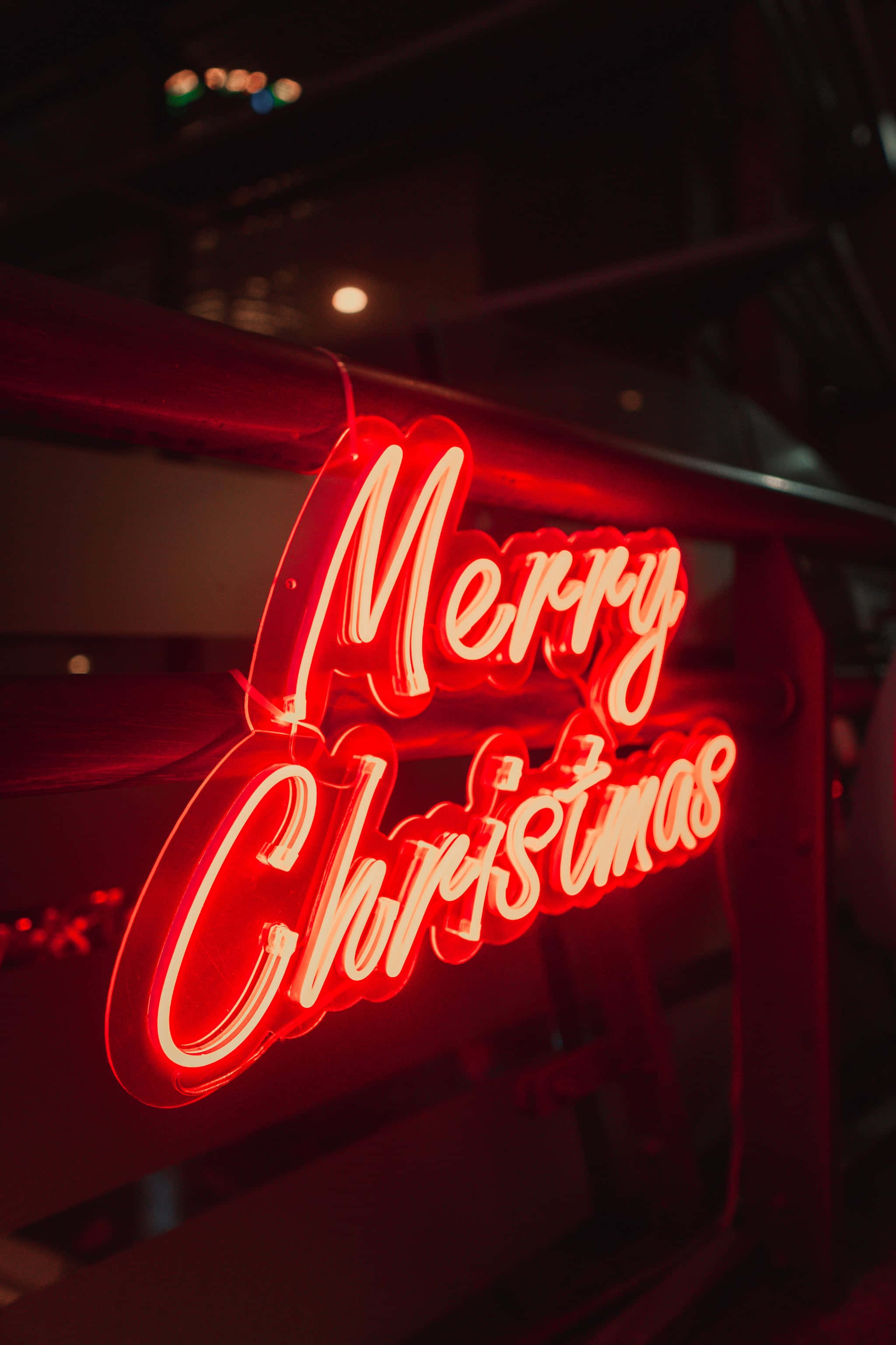 美學 桌布 壁紙 — 一個發光的紅色霓虹燈牌寫著 Merry Christmas，在黑暗的城市夜景背景下投射出溫暖的節日光芒。