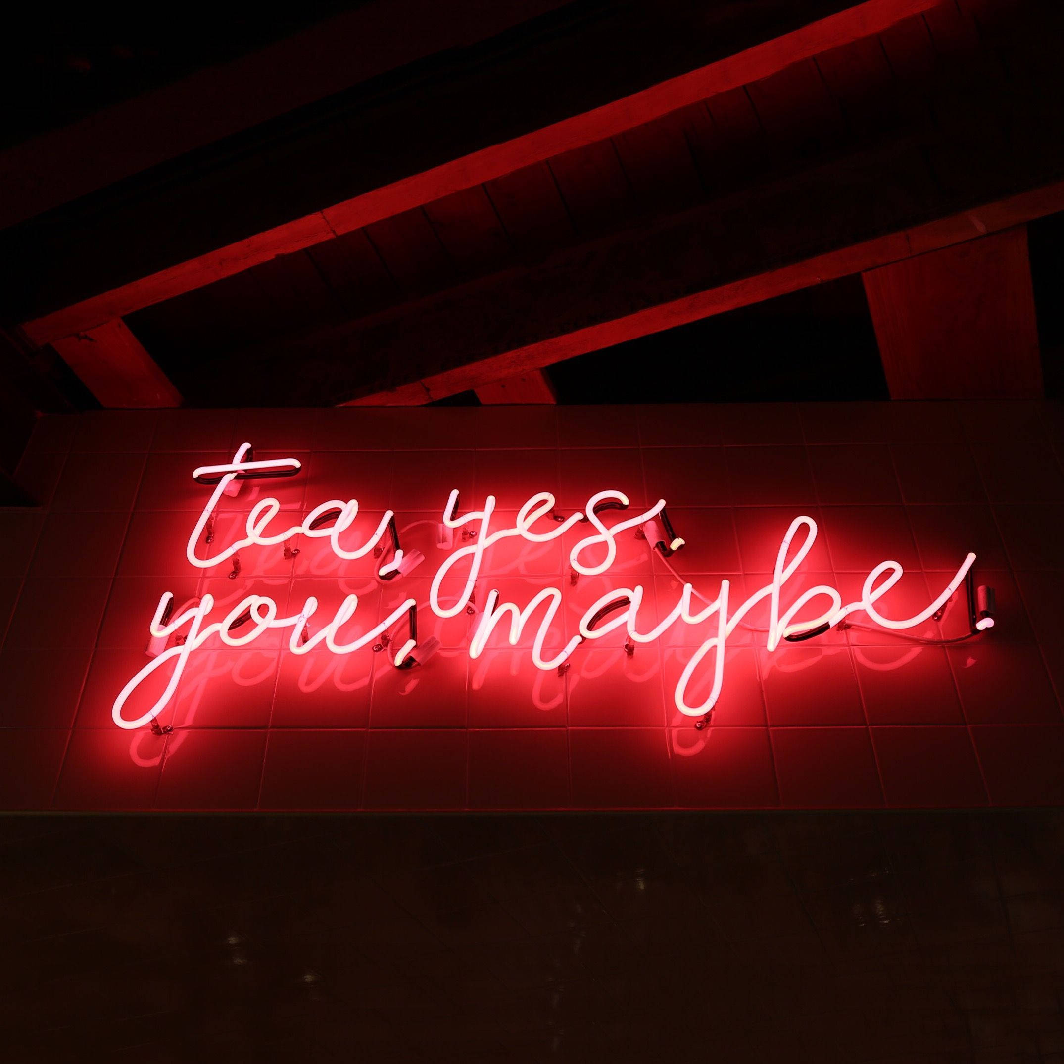 美學 桌布 壁紙 — 一個發光的紅色霓虹燈牌寫著 tea yes you maybe，背景是木樑下的深色磁磚牆。