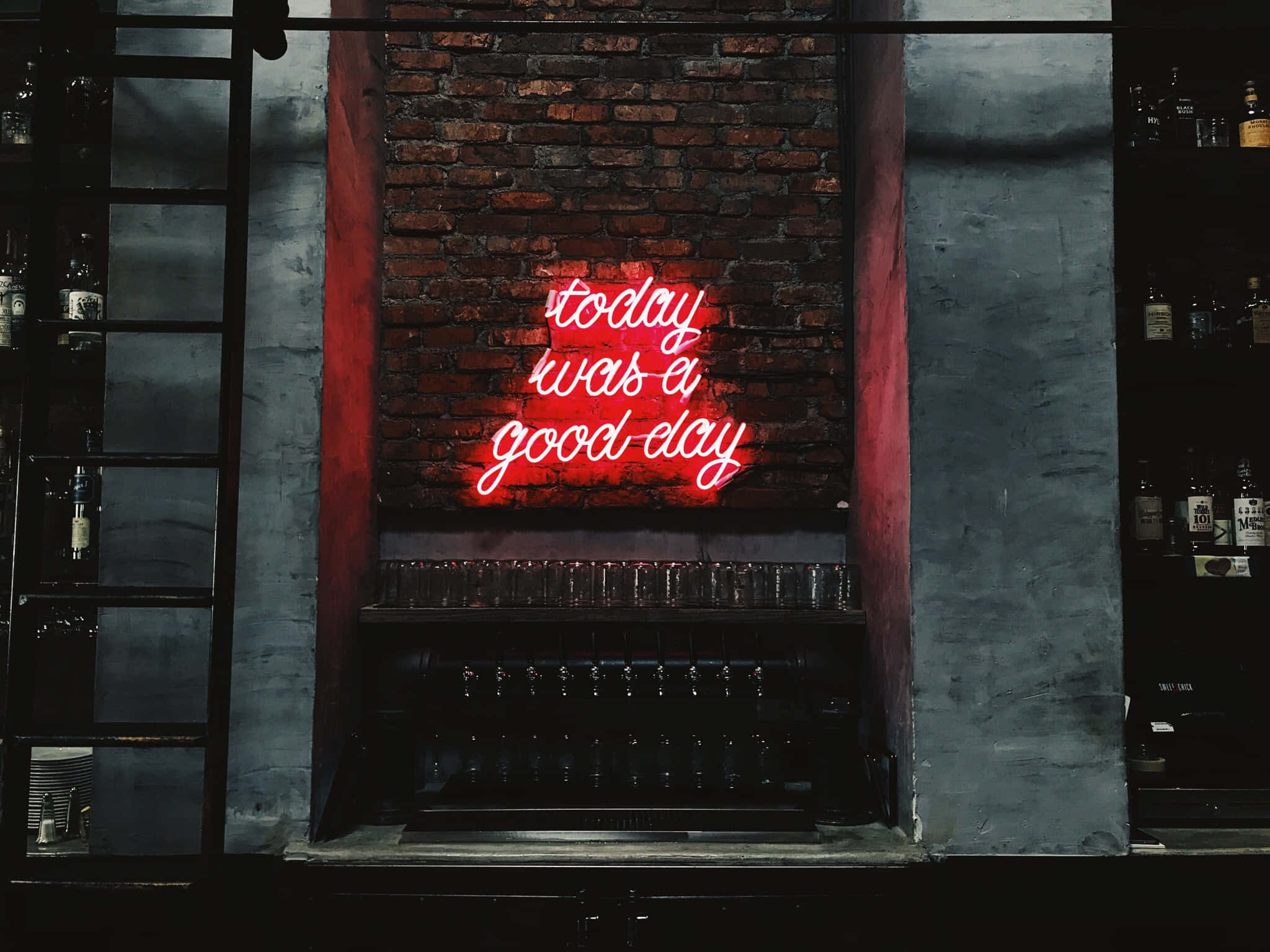 Minimalist Quote 桌布 壁紙 — 一個發光的紅色霓虹燈牌寫著「today was a good day」，照亮了酒吧後面的磚牆，酒吧上有玻璃杯和酒瓶。