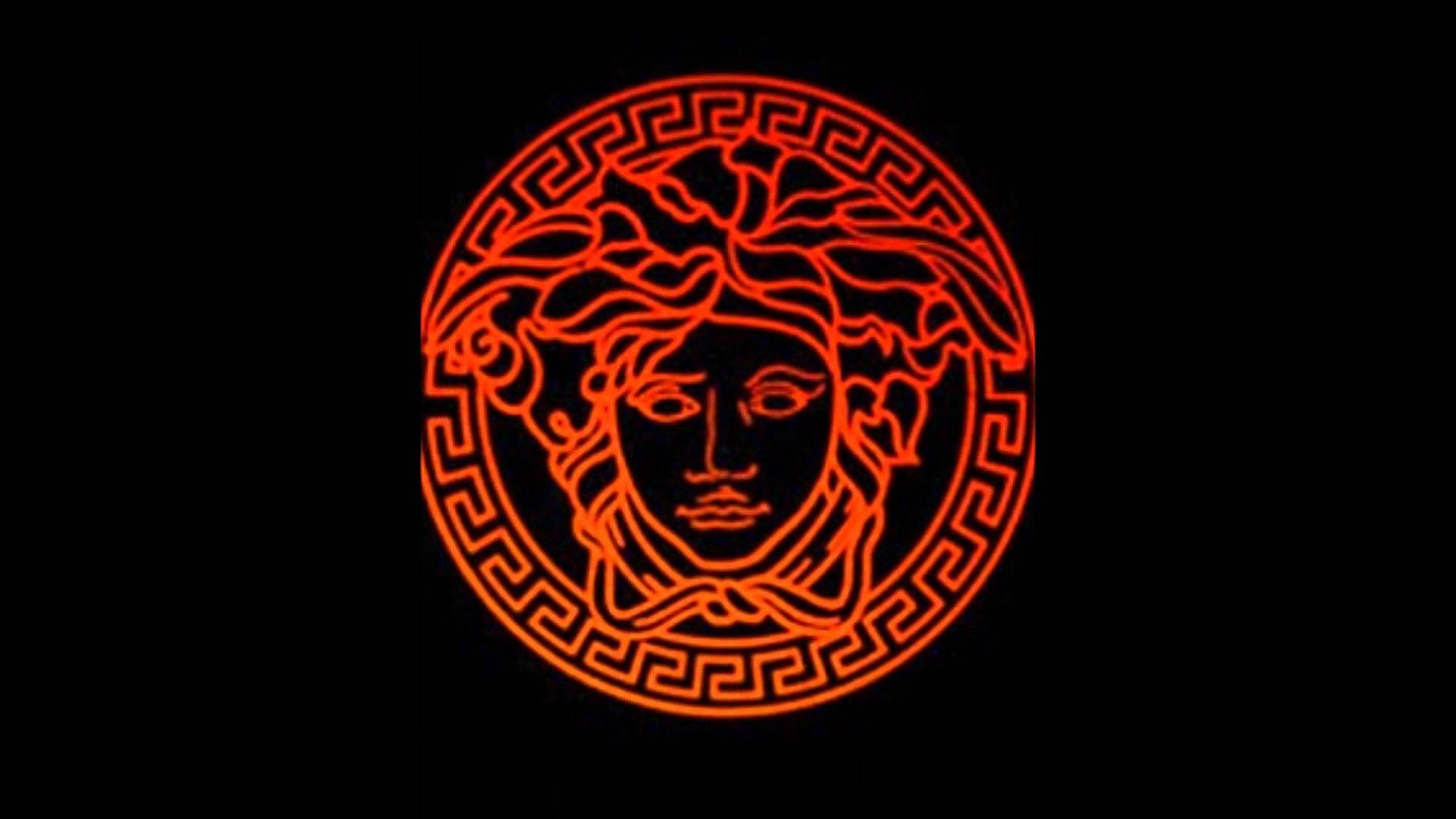Versace Logo 桌布 壁紙 — 一個發光的紅色霓虹燈美杜莎頭標誌，帶有希臘鑰匙邊框，背景為黑色。