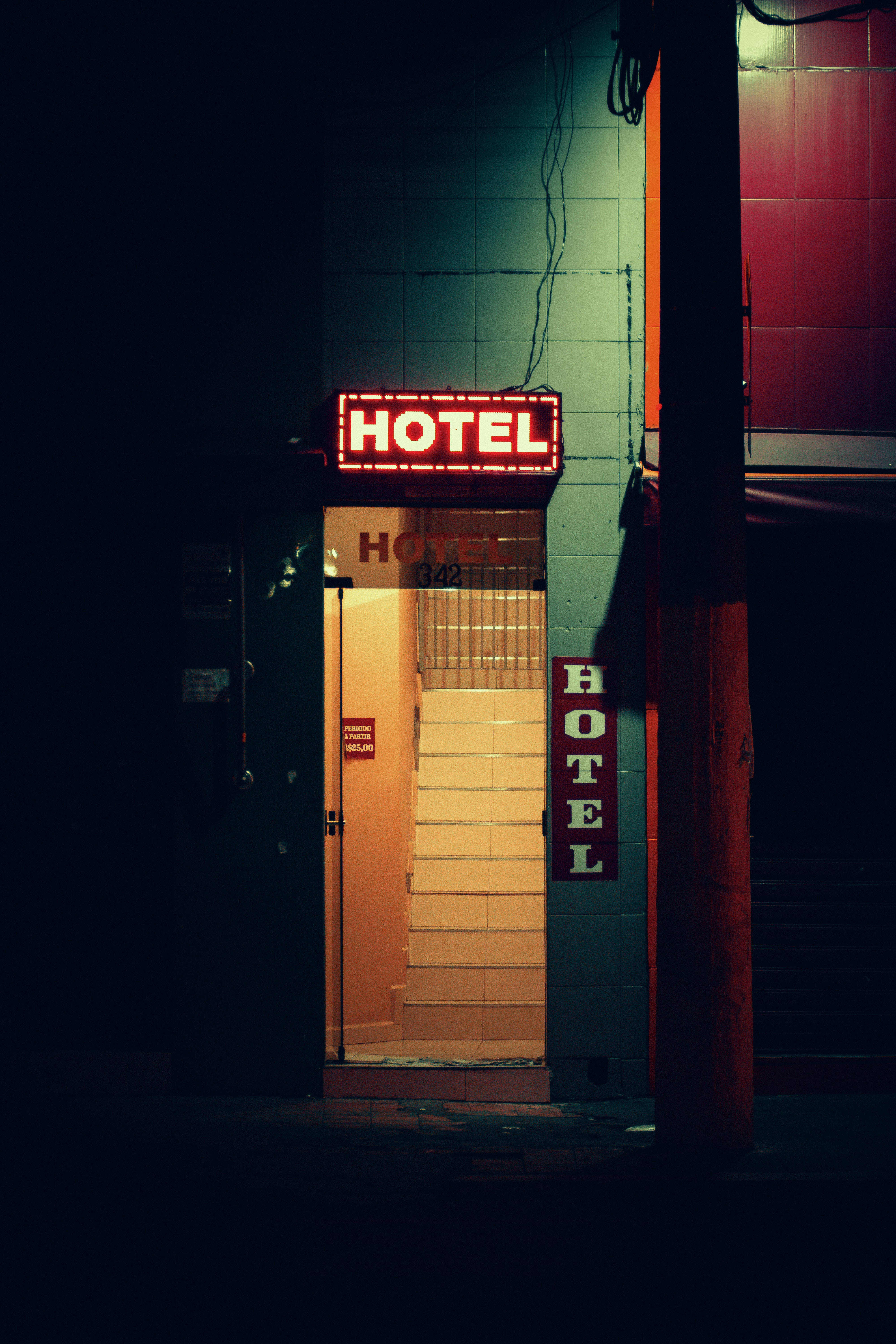 Hotel 桌布 壁紙 — 一個發光的紅色霓虹燈酒店招牌在夜晚照亮了一條狹窄的小巷，將溫暖的光線投射在瓷磚樓梯和黑暗的牆壁上。