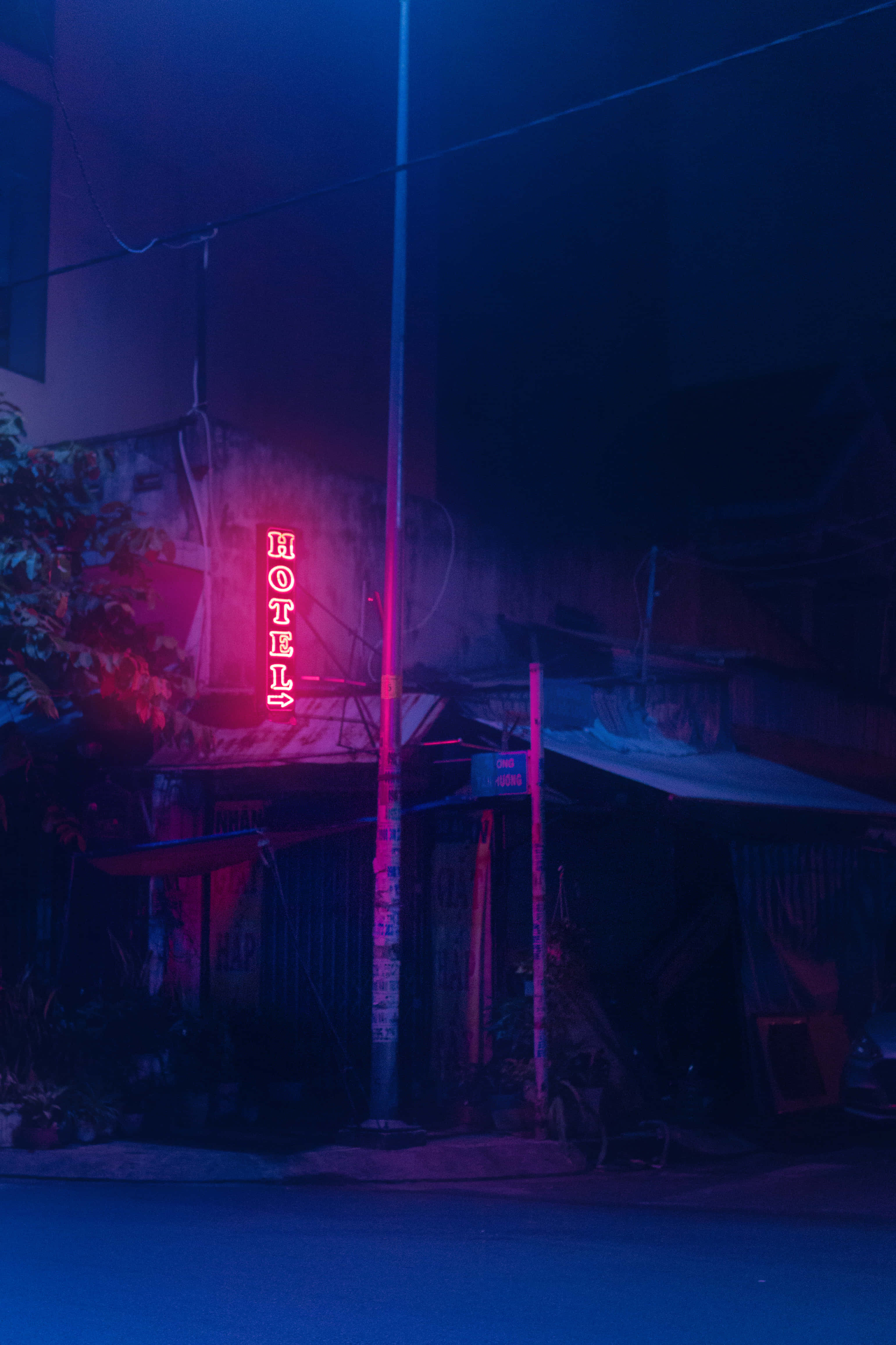 氛圍 桌布 壁紙 — 一個發光的紅色霓虹燈酒店招牌在夜晚將鮮豔的粉紅色和藍色光投射在風化的城市小巷中。