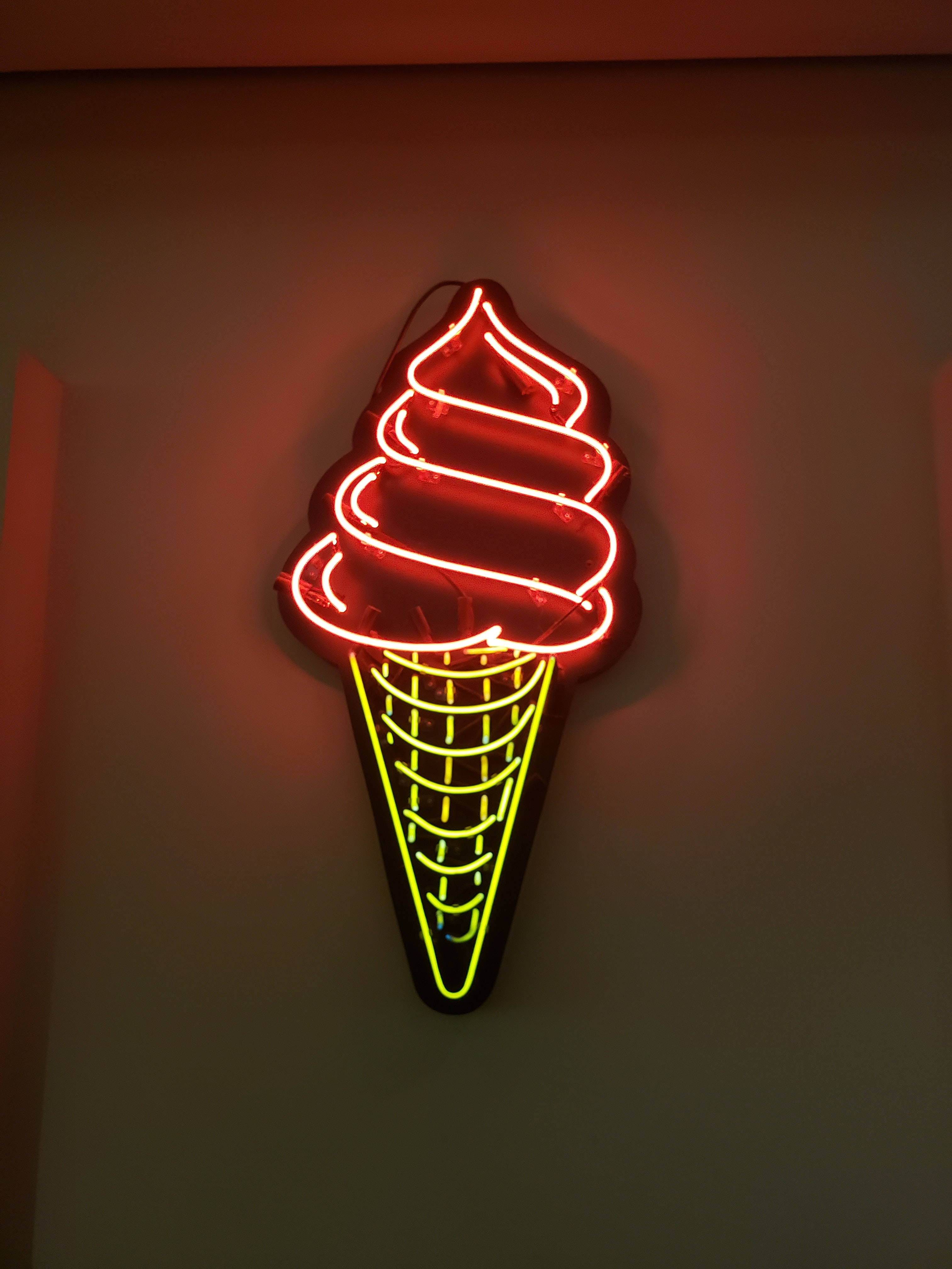 Ice Cream 桌布 壁紙 — 一個發光的紅黃色霓虹燈牌，形狀像一個扭曲的冰淇淋甜筒，安裝在昏暗的牆上。