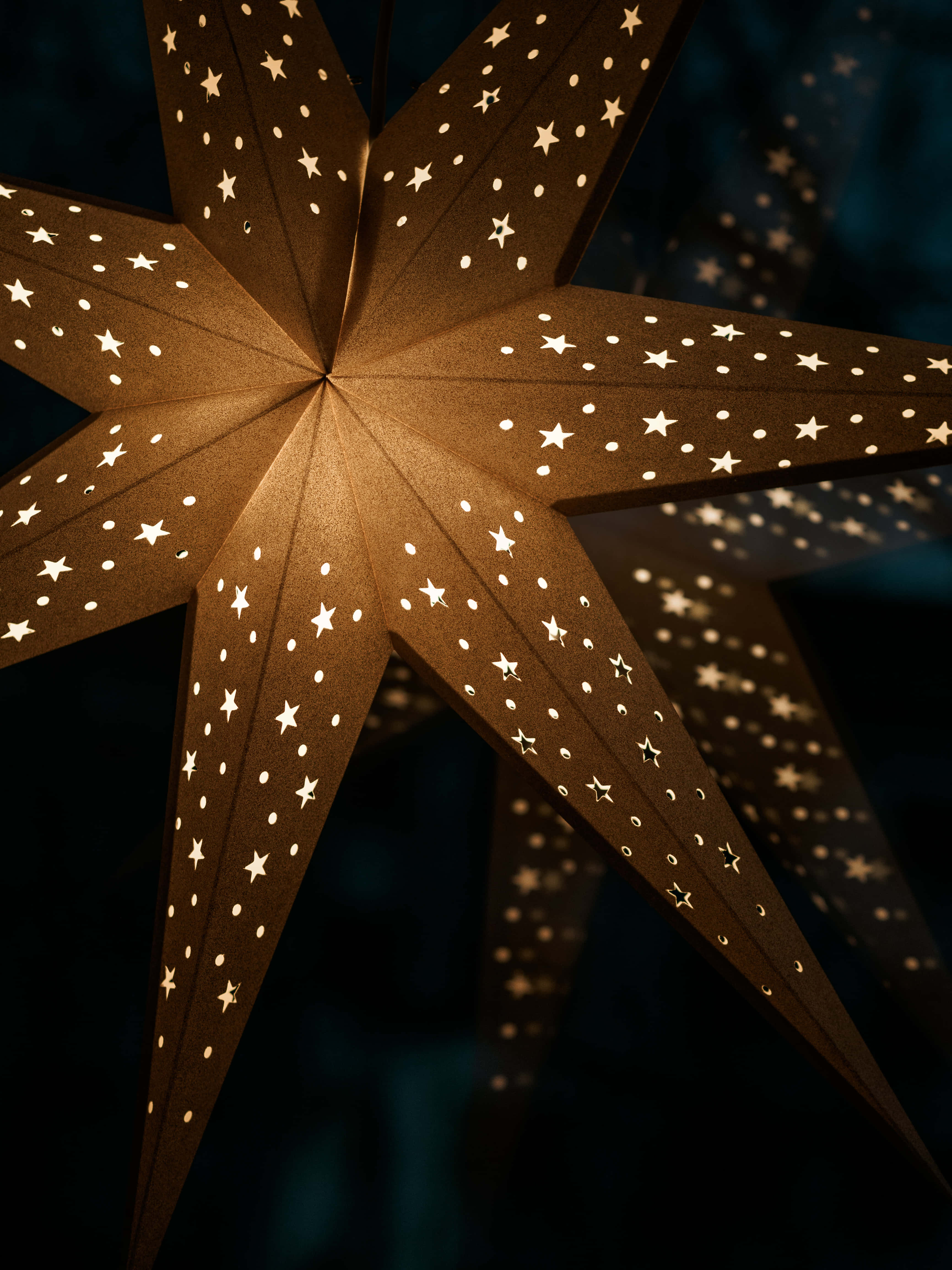 Christmas Star 桌布 壁紙 — 一個發光的紙星星燈籠，帶有星星和圓點鏤空，在黑暗背景下投射出溫暖的光芒。