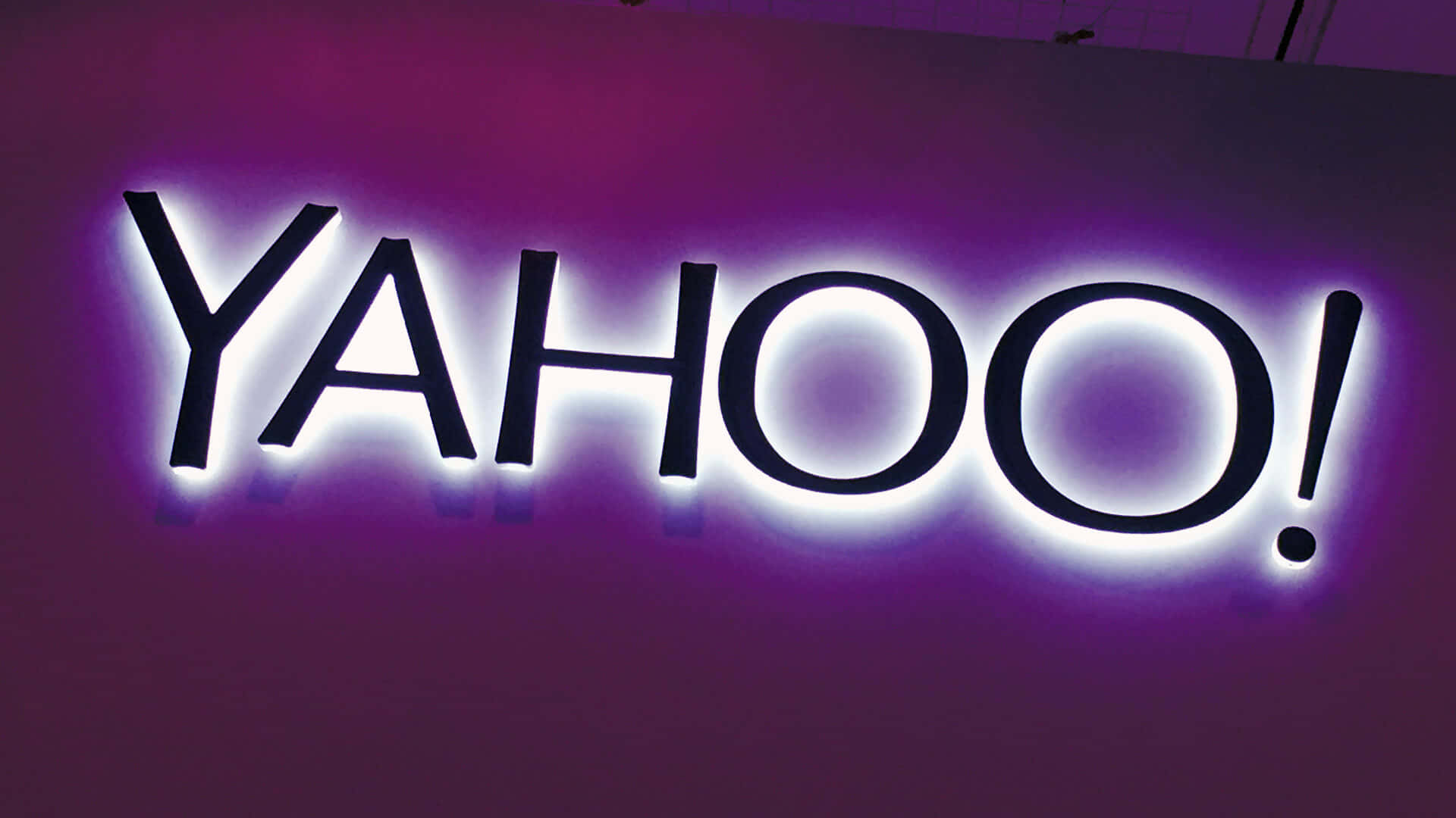 Yahoo 桌布 壁紙 — 一個發光的紫色和白色Yahoo標誌招牌，在黑暗的牆壁上帶有明亮的背光。