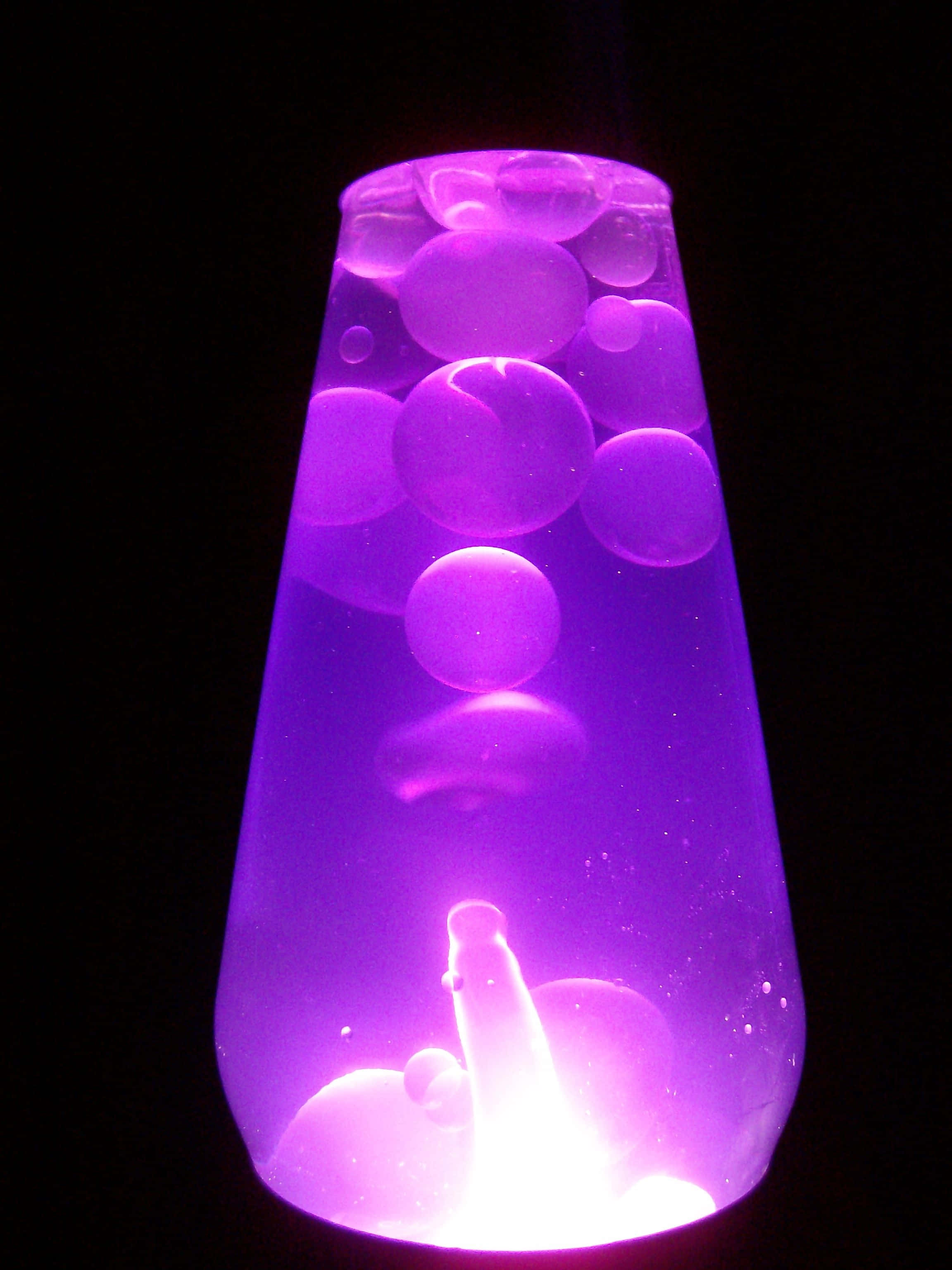 lava lamp 桌布 壁紙 — 一個發光的紫色熔岩燈，帶有浮動的氣泡，在黑色背景上照亮。