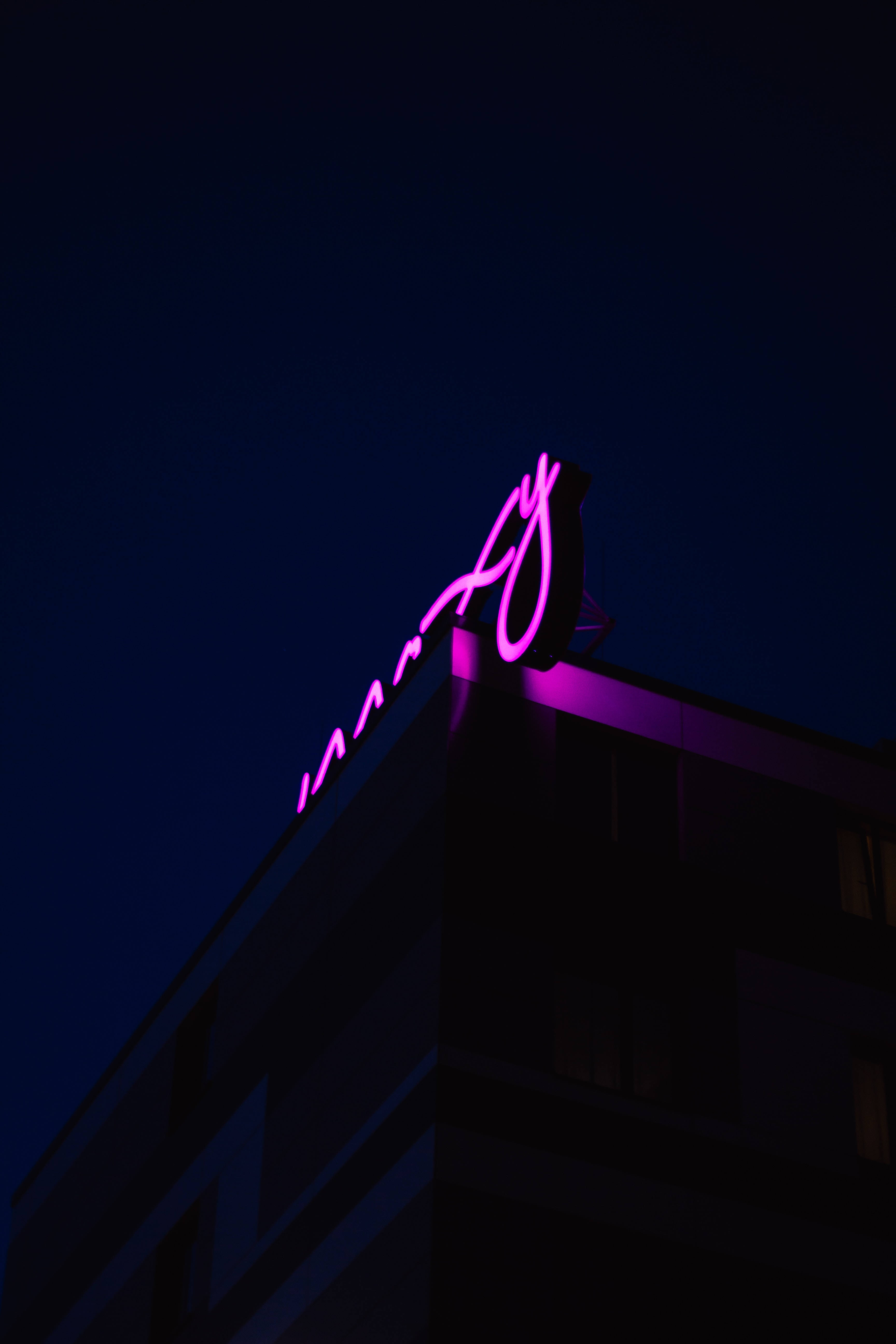 neon sign 桌布 壁紙 — 一個發光的紫色霓虹燈招牌在黑暗的建築物上彎曲，襯托著深邃的夜空。