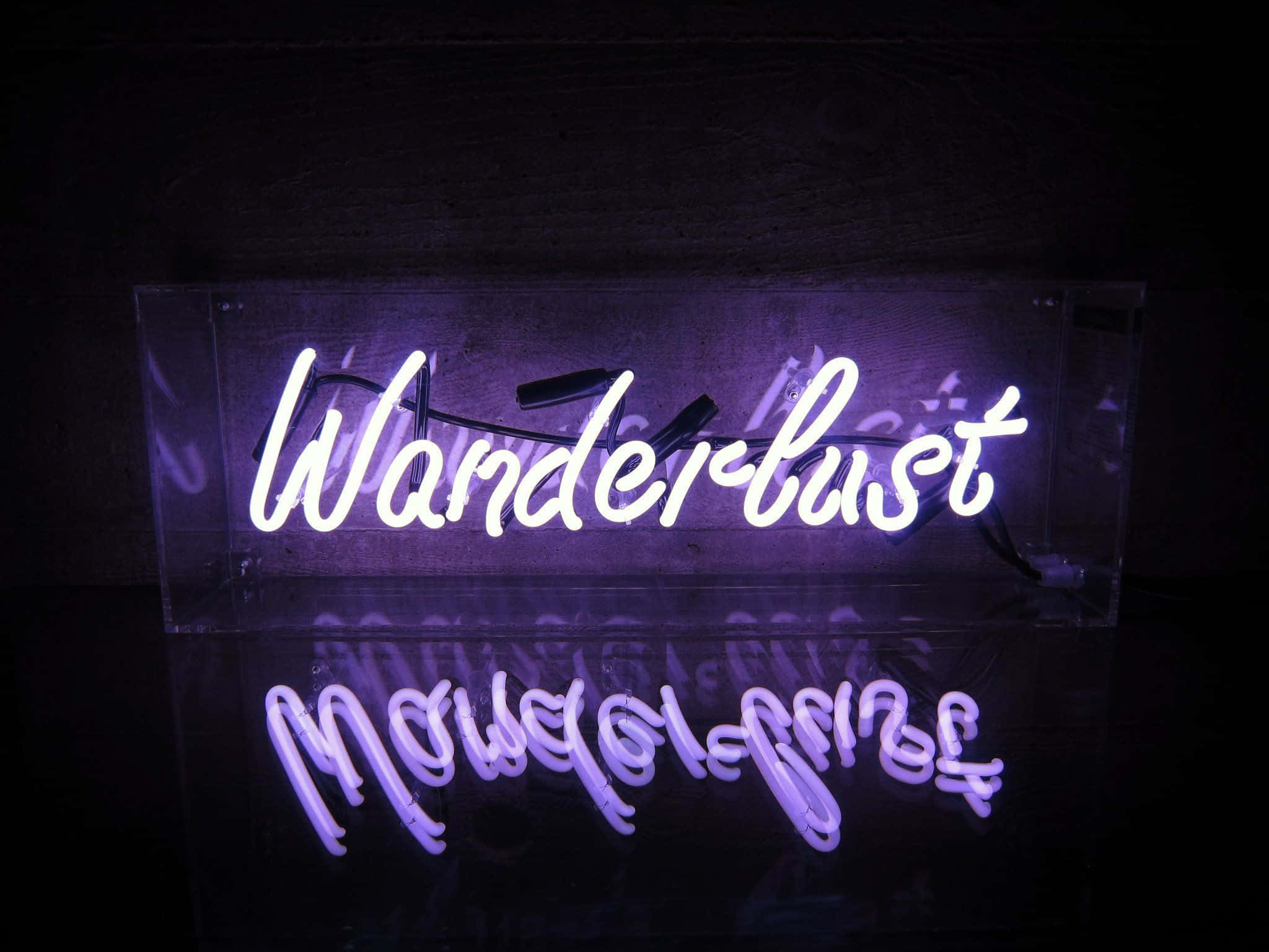 語錄 桌布 壁紙 — 一個發光的紫色霓虹燈牌，上面寫著「Wanderlust」，在深色光滑表面上投射出柔和倒影。