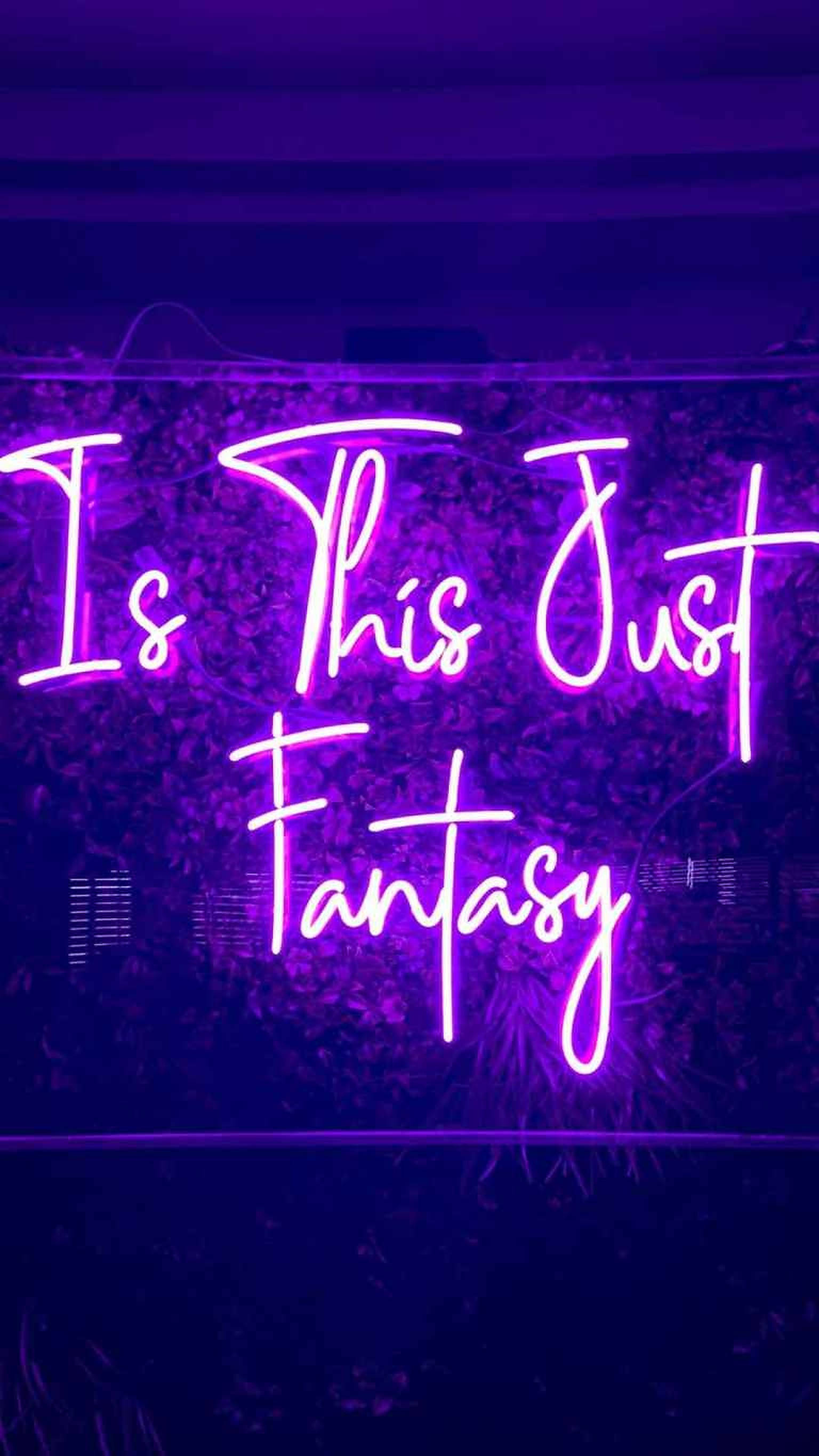 LED 桌布 壁紙 — 一個發光的紫色霓虹燈牌在深色紋理牆上寫著「Is This Just Fantasy」。
