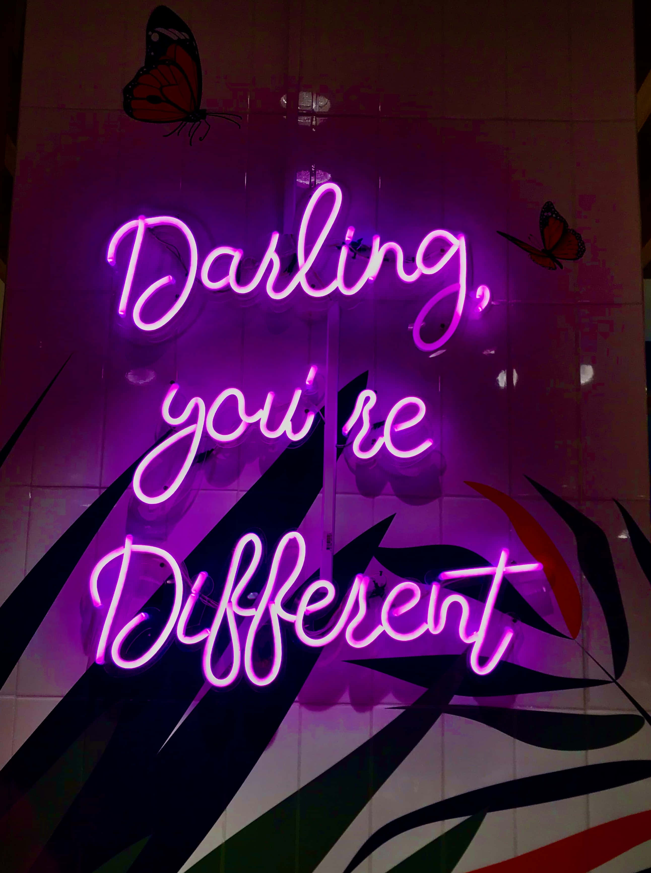 Purple Neon 桌布 壁紙 — 一個發光的紫色霓虹燈牌在磁磚牆上寫著 Darling you're Different，牆上有蝴蝶貼紙和葉子圖案。