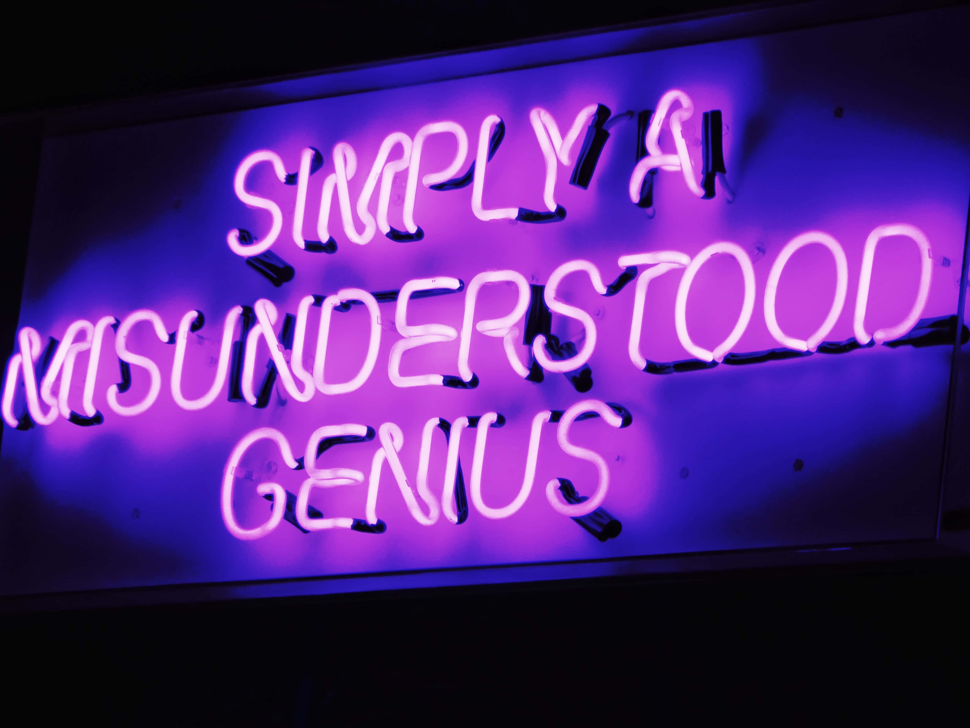 Purple Neon 桌布 壁紙 — 一個發光的紫色霓虹燈牌在黑暗背景上寫著「只是一個被誤解的天才」。