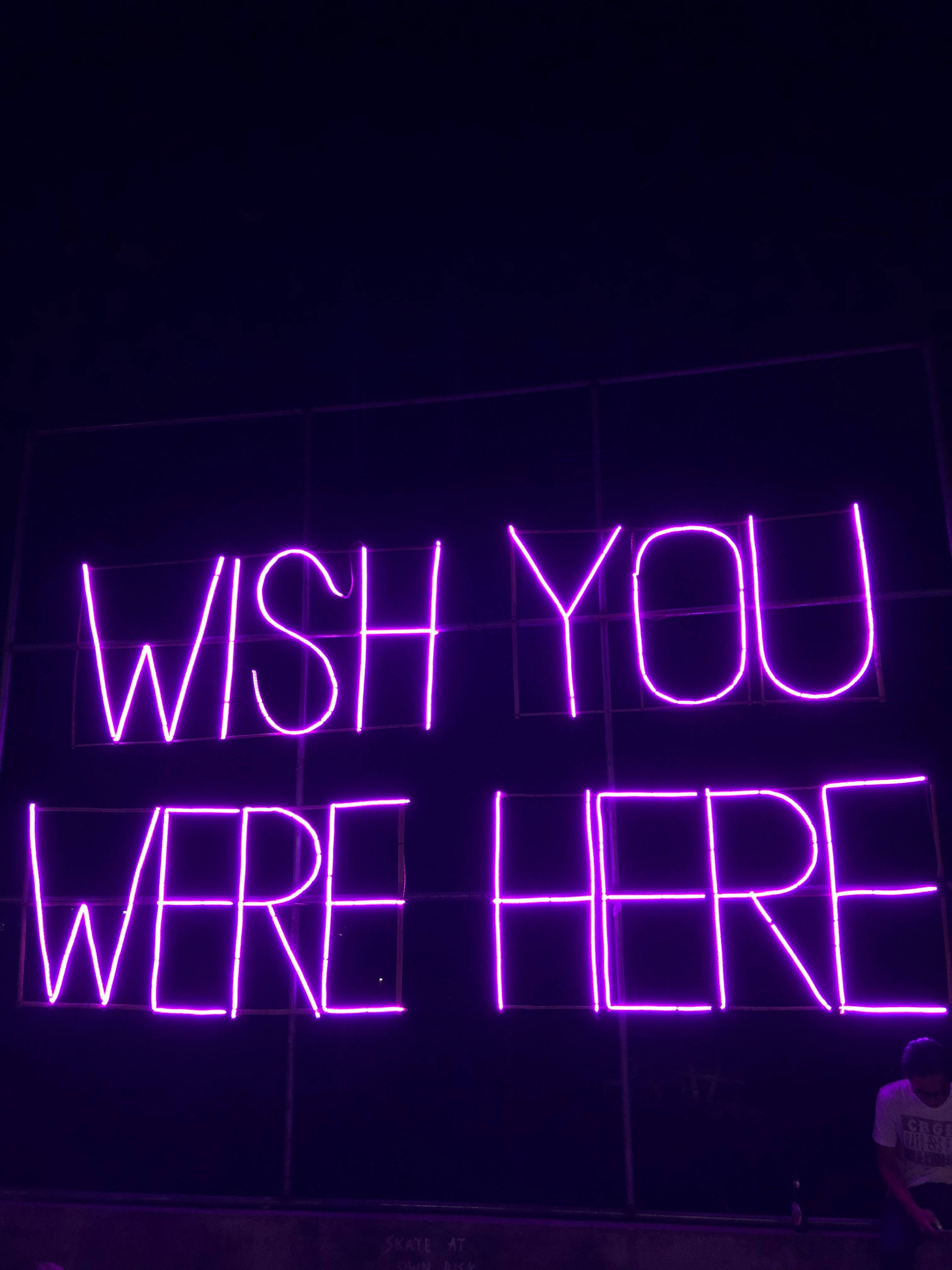 霓虹紫 iPhone 桌布 壁紙 — 一個發光的紫色霓虹燈牌寫著「WISH YOU WERE HERE」，背景是漆黑的夜空，下方隱約可見一個人。