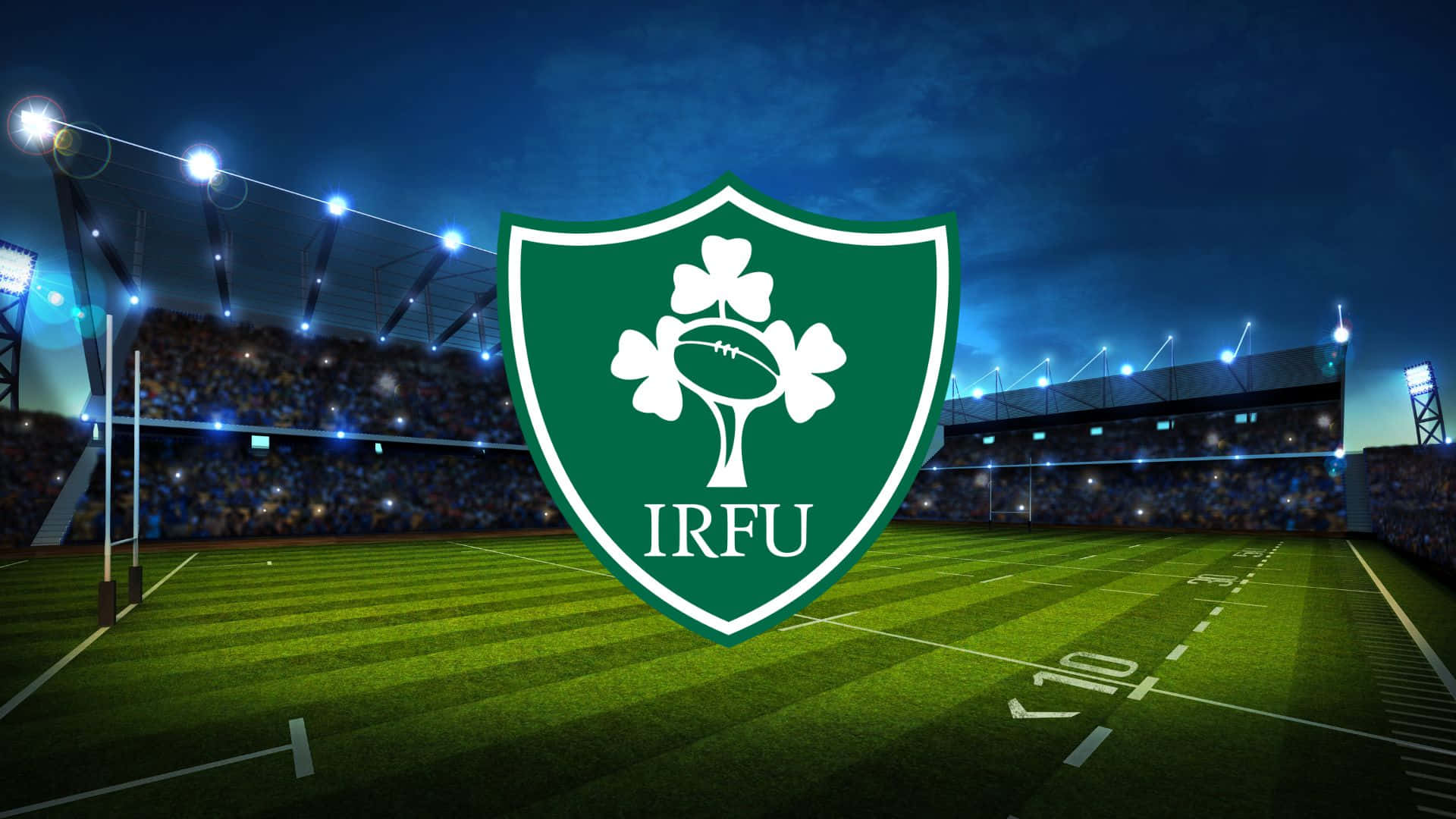 Ireland Rugby 桌布 壁紙 — 一個發光的綠色IRFU盾牌，帶有三葉草和橄欖球，在夜間主導了明亮的橄欖球場。