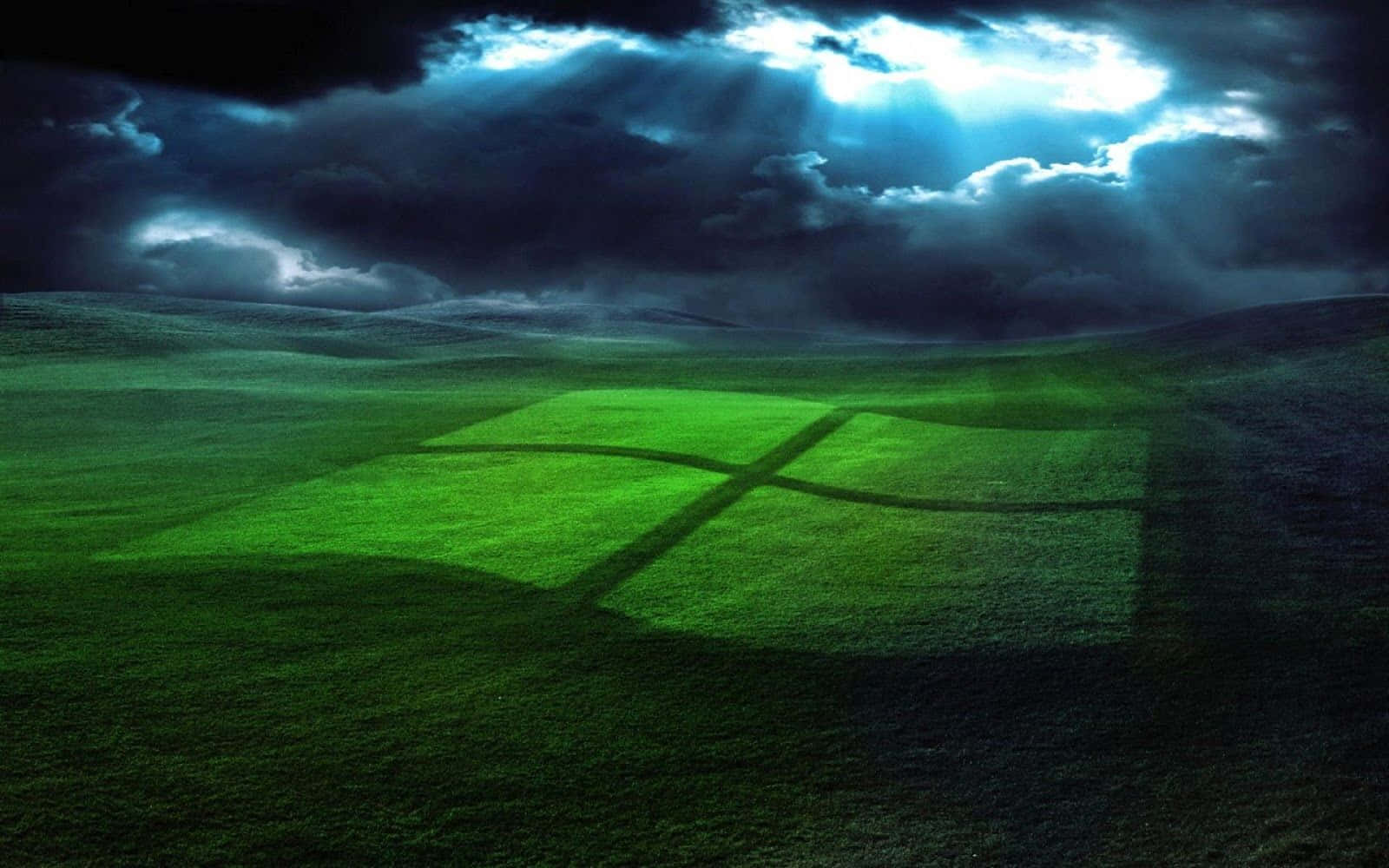 Windows XP 桌布 壁紙 — 一個發光的綠色Windows標誌刻在草地上，背景是戲劇性的暴風雨天空，陽光穿透雲層。