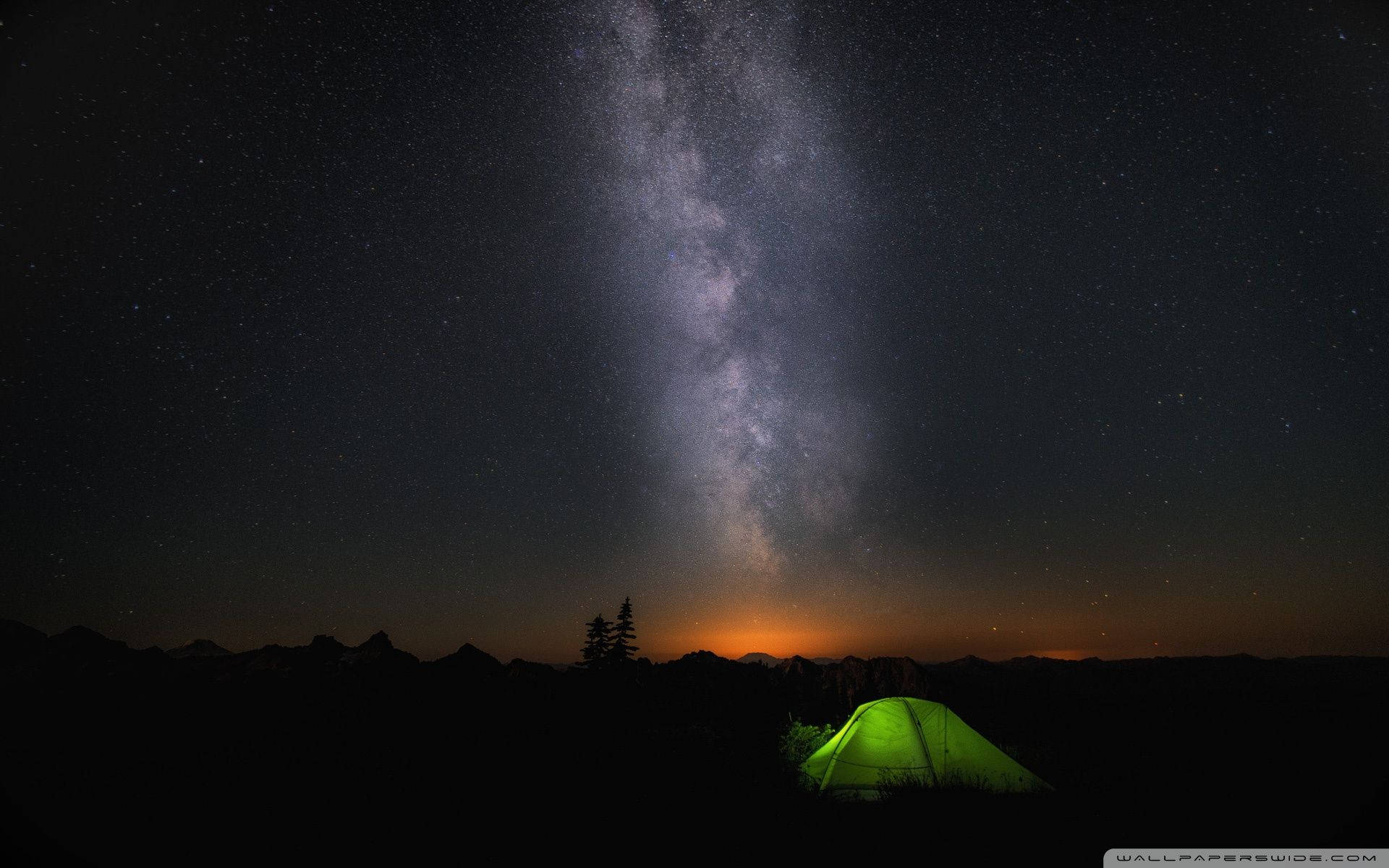 夜空 桌布 壁紙 — 一個發光的綠色帳篷坐落在令人嘆為觀止的銀河系之下，銀河在星空夜空中拱起，越過剪影山脈。