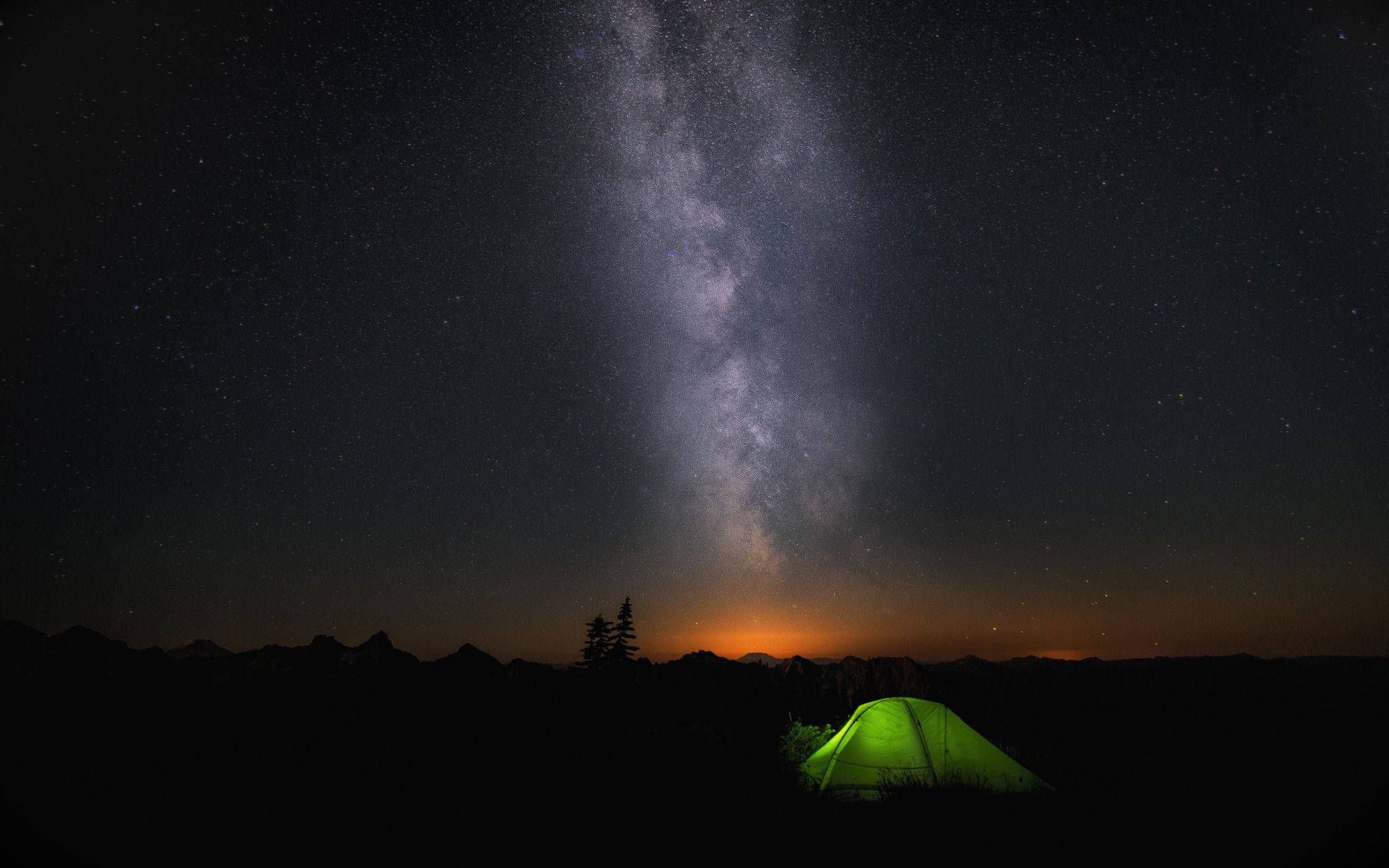 Stars 桌布 壁紙 — 一個發光的綠色帳篷獨自矗立在令人驚嘆的銀河之下，銀河在夜晚彎曲在黑暗的山脈之上。