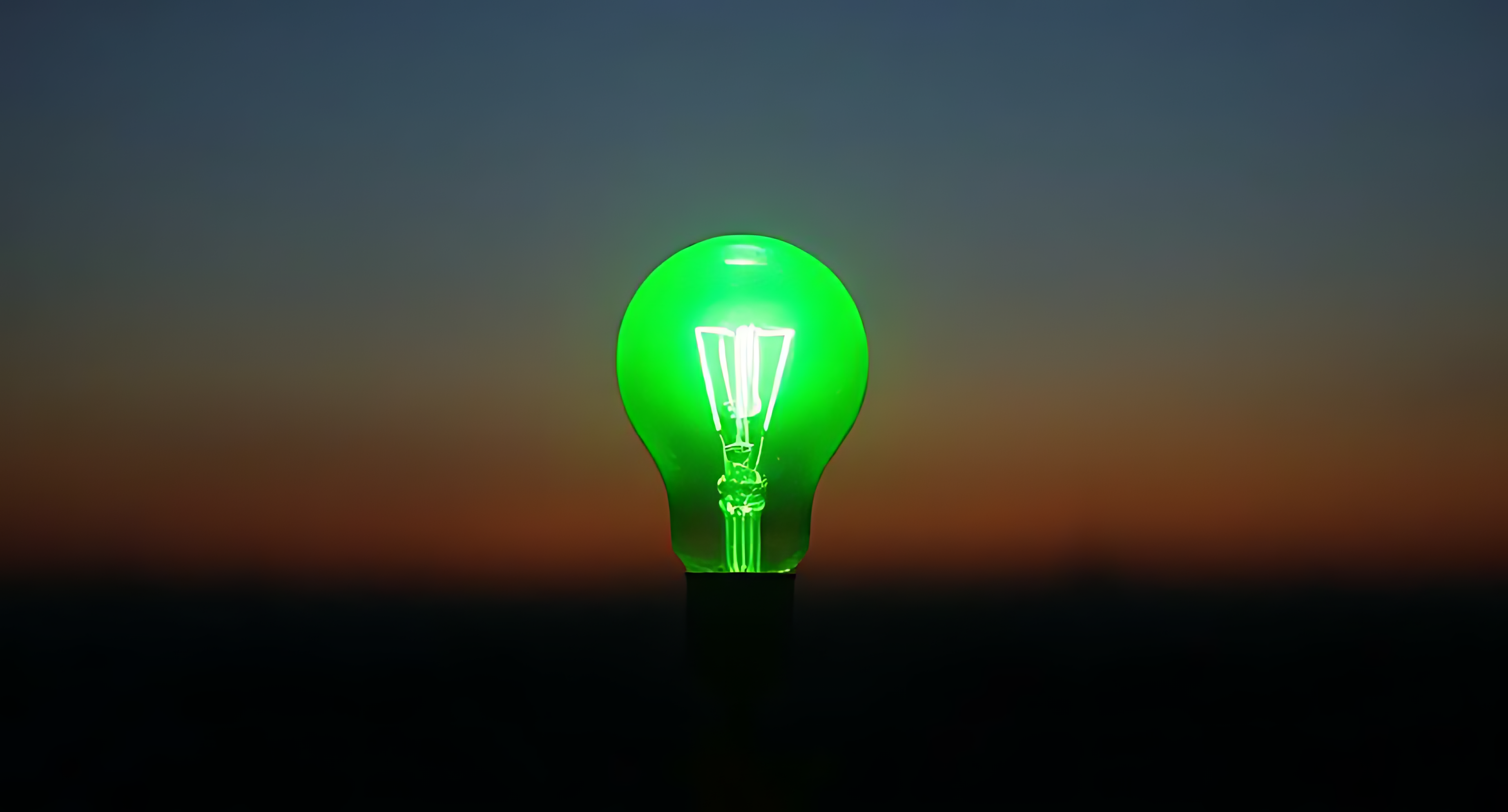 Bulb 桌布 壁紙 — 一個發光的綠色復古燈泡獨自矗立在從橙色漸變到深藍色的暮色天空中。