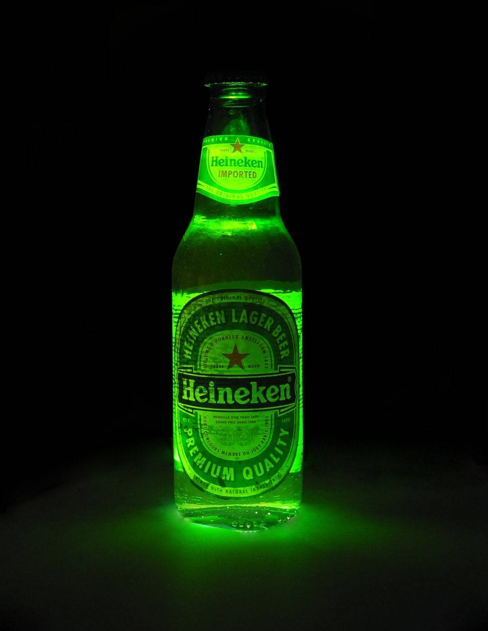 Drink 桌布 壁紙 — 一個發光的綠色海尼根啤酒瓶在漆黑的背景下散發出光芒。