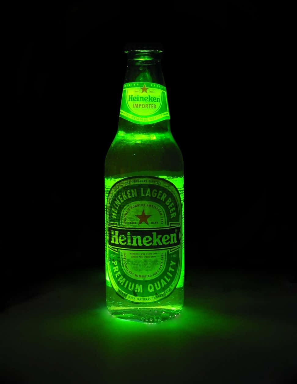 Heineken 桌布 壁紙 — 一個發光的綠色海尼根啤酒瓶在漆黑的背景下散發出光芒，在下方表面投射出鮮豔的綠色光暈。