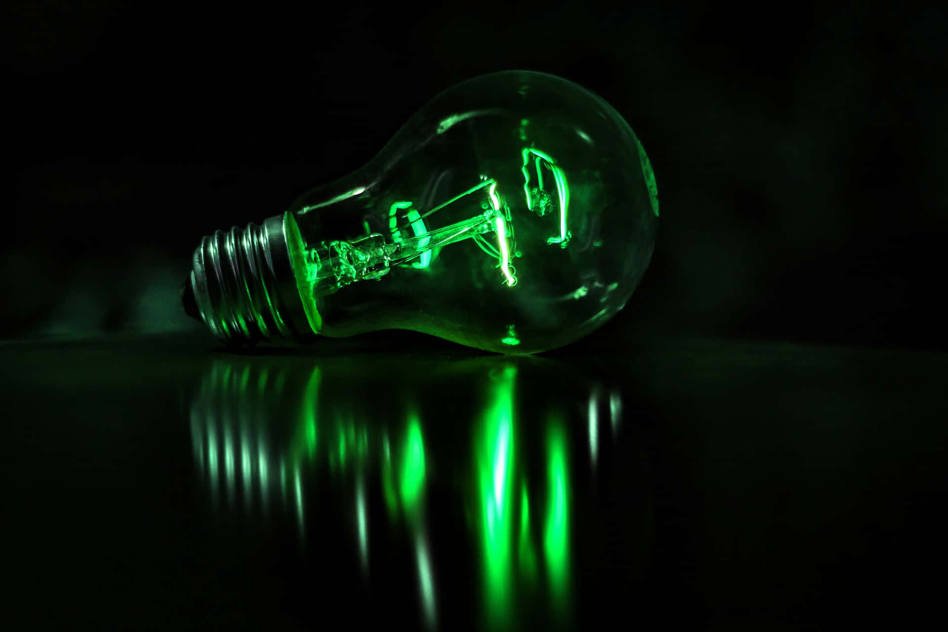 Green Led 桌布 壁紙 — 一個發光的綠色燈泡放在反光表面上，在黑暗背景下投射出鮮豔的綠色反射。